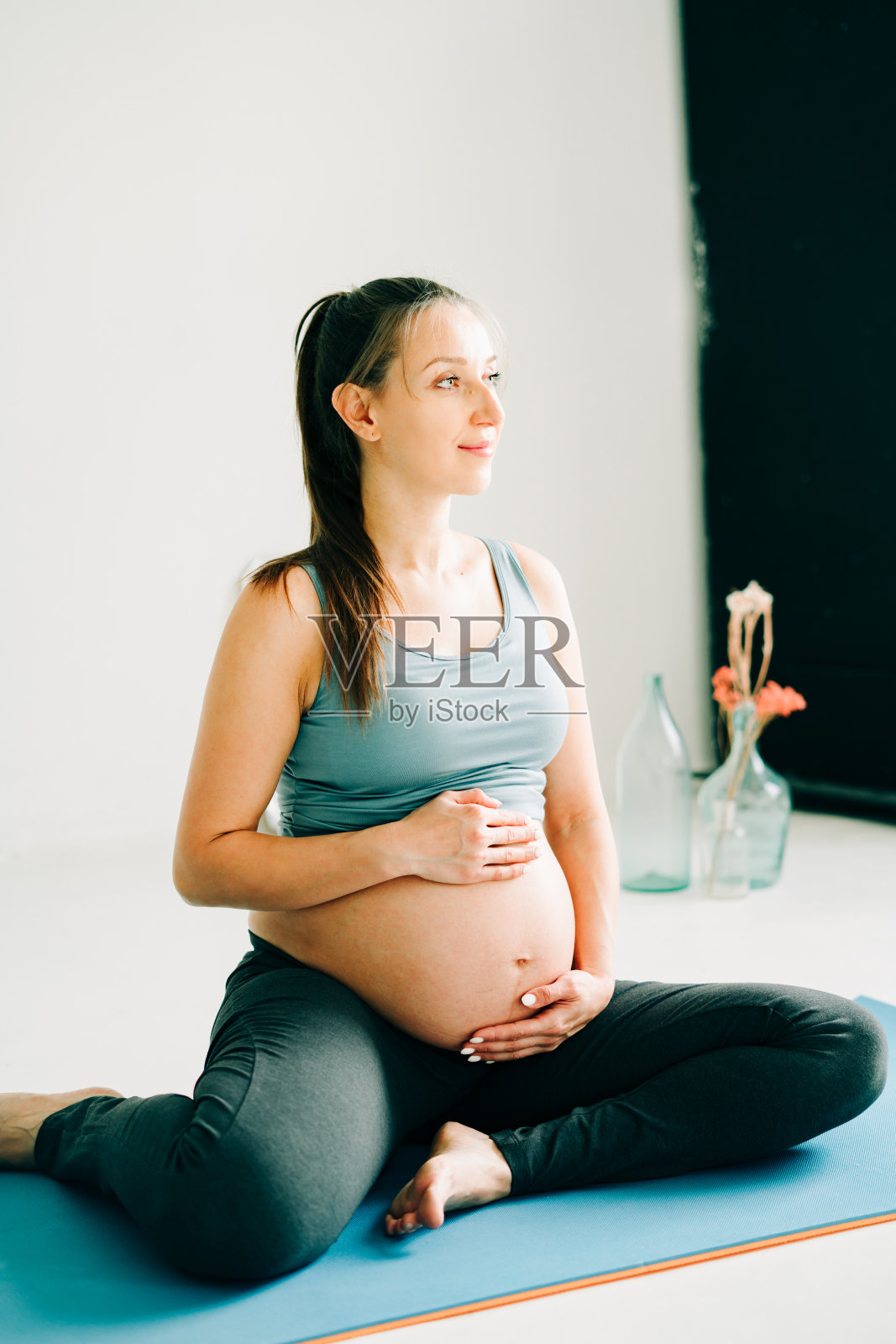 穿着运动服的孕妇坐在瑜伽垫上抚摸肚子照片摄影图片