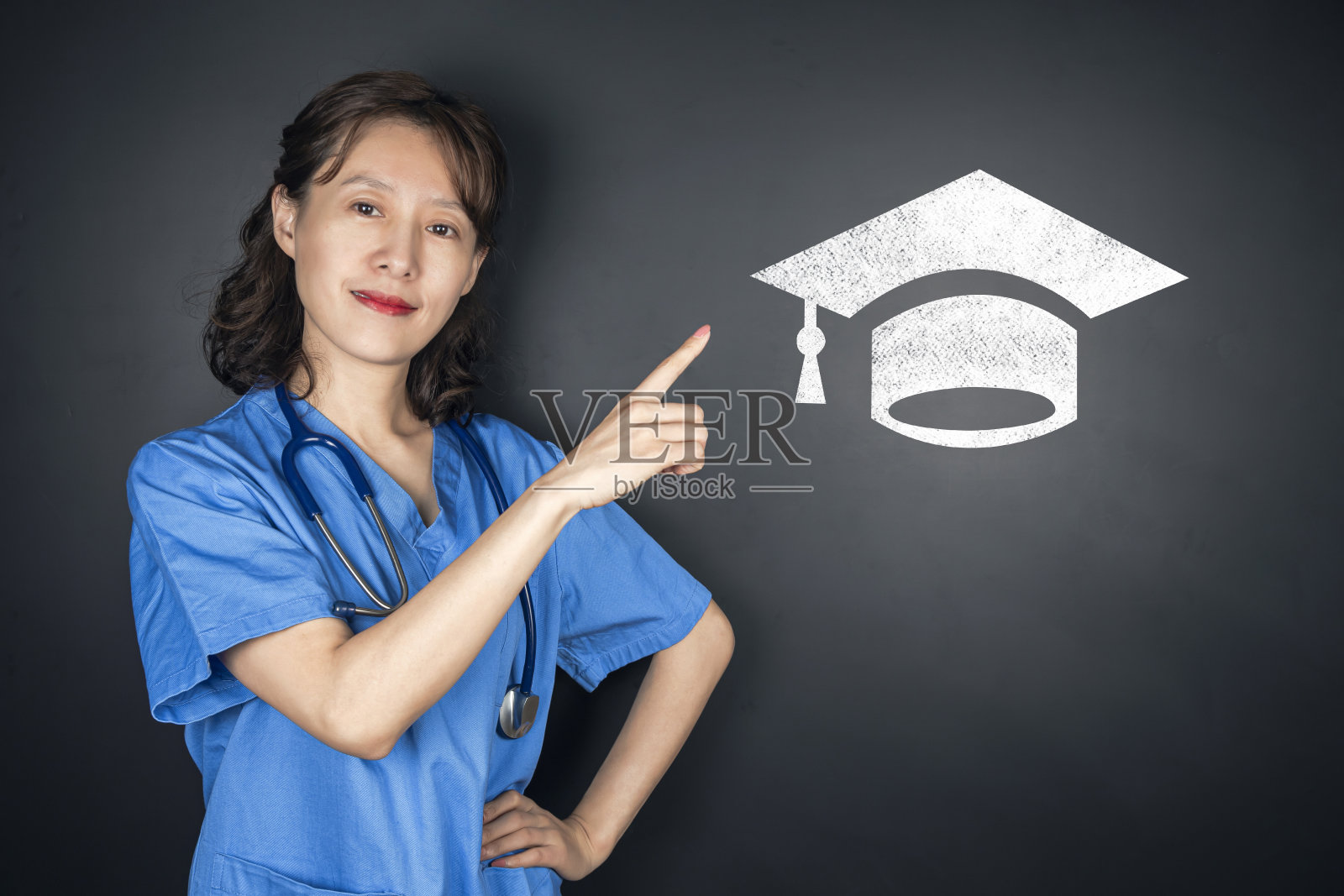 美丽年轻亚洲医生指向黑板上的学士帽照片摄影图片