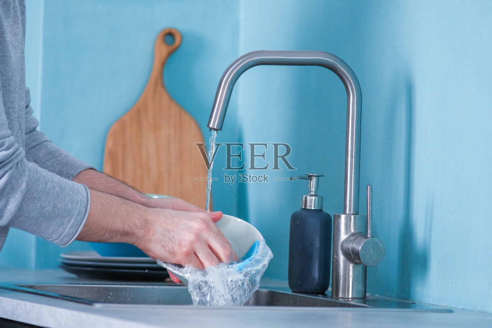 一个男人在厨房里用蓝色的生态海绵洗盘子，厨房的墙壁是蓝色的照片摄影图片