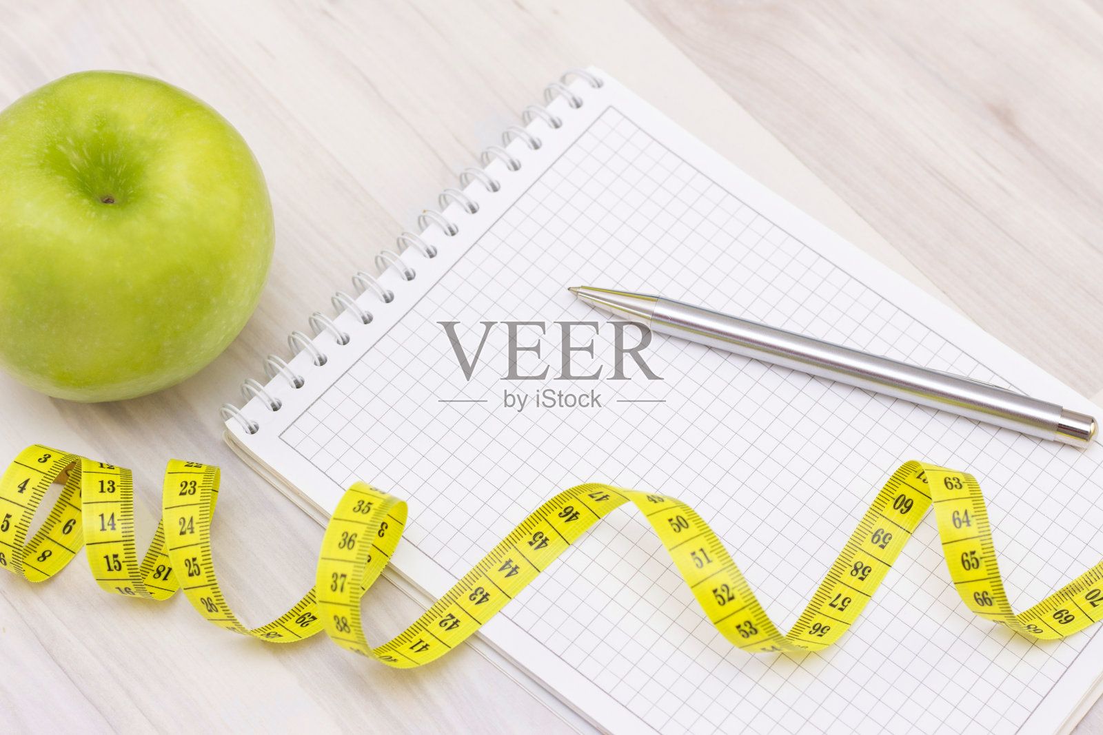 秤，一个青苹果，卷尺和一个在轻木背景上写字的笔记本。准备夏季和海滩的季节，减肥和运动的概念照片摄影图片