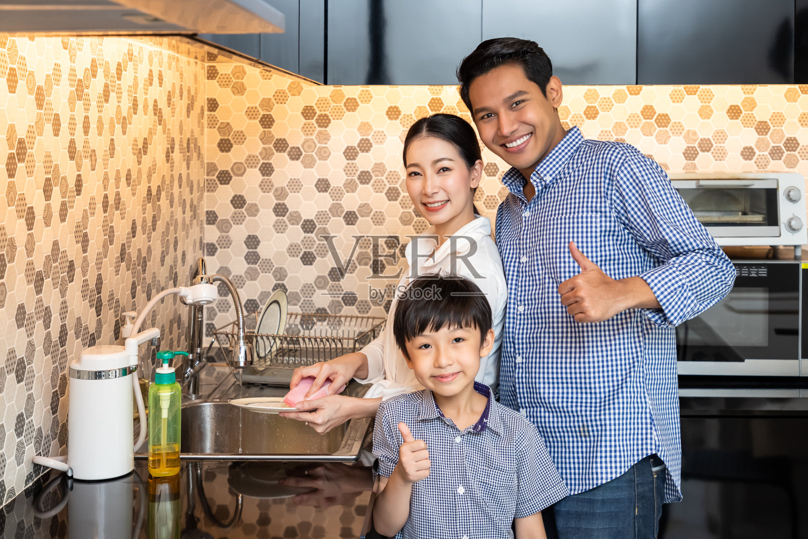 年轻的亚洲母亲和丈夫儿子在现代厨房洗碗，看着镜头竖起大拇指照片摄影图片
