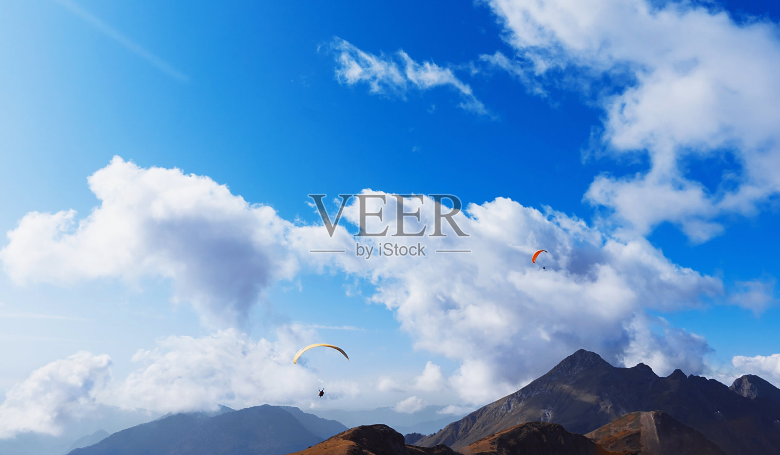 在一个晴朗的夏日，滑翔伞飞过群山。跳伞运动的概念。照片摄影图片