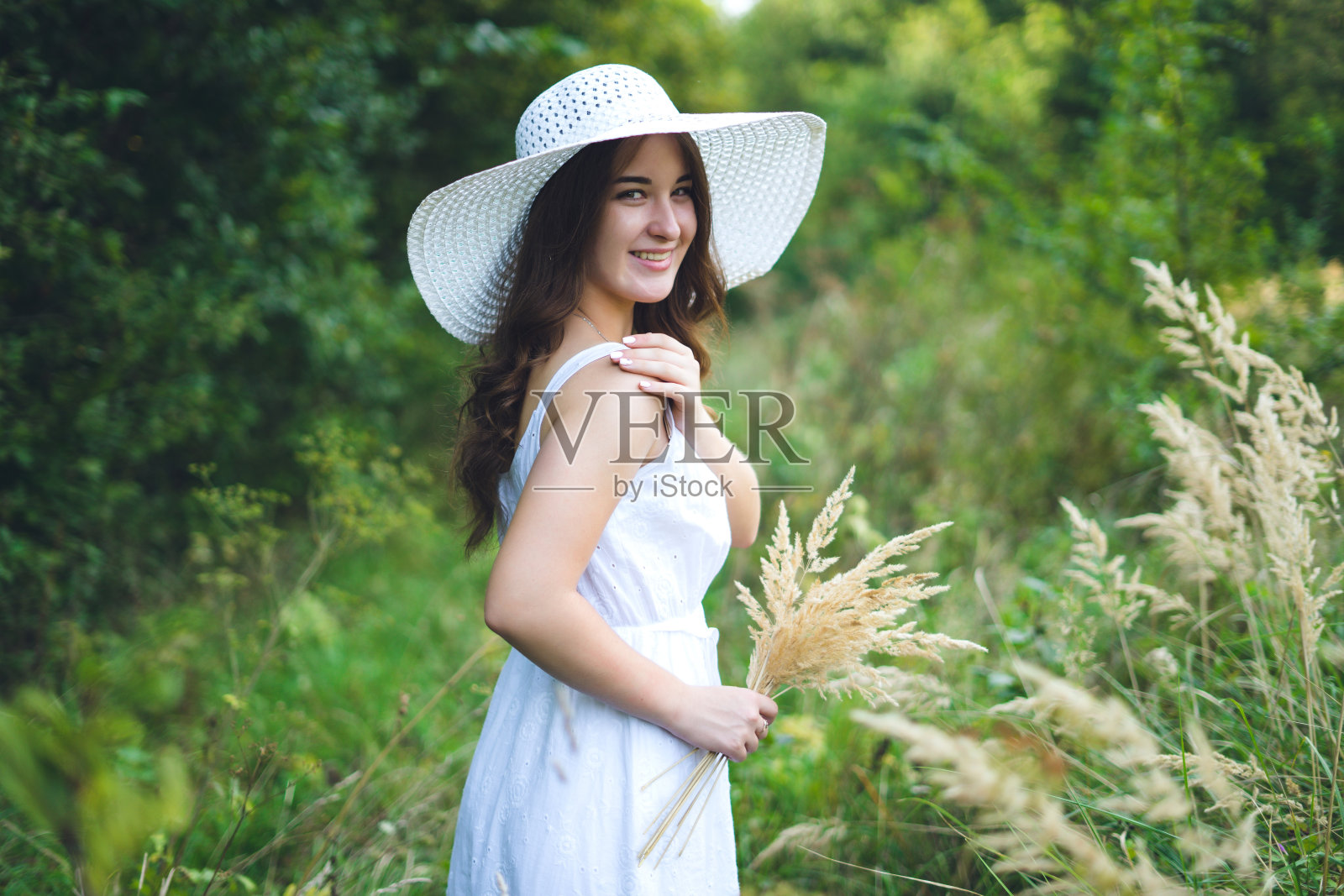 年轻美丽的女子肖像穿着白色的连衣裙，侧身，户外夏日的森林里。年轻女孩在夏日公园散步照片摄影图片