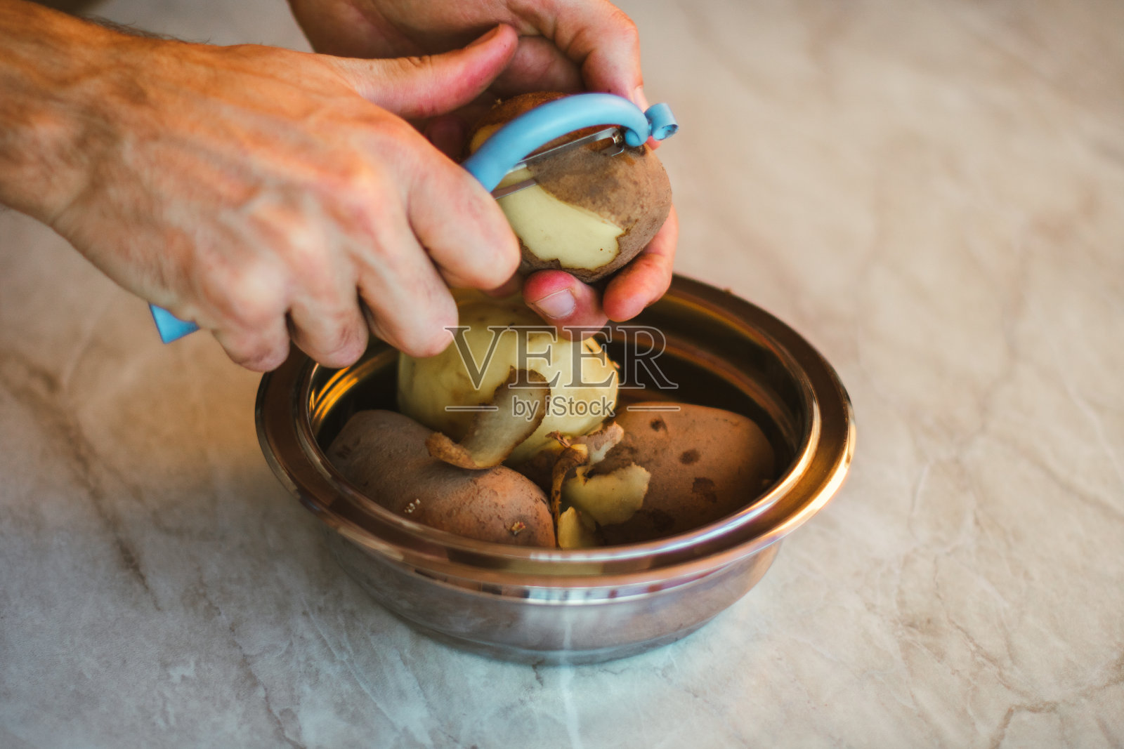 一个人正在厨房的金属锅里削土豆皮照片摄影图片