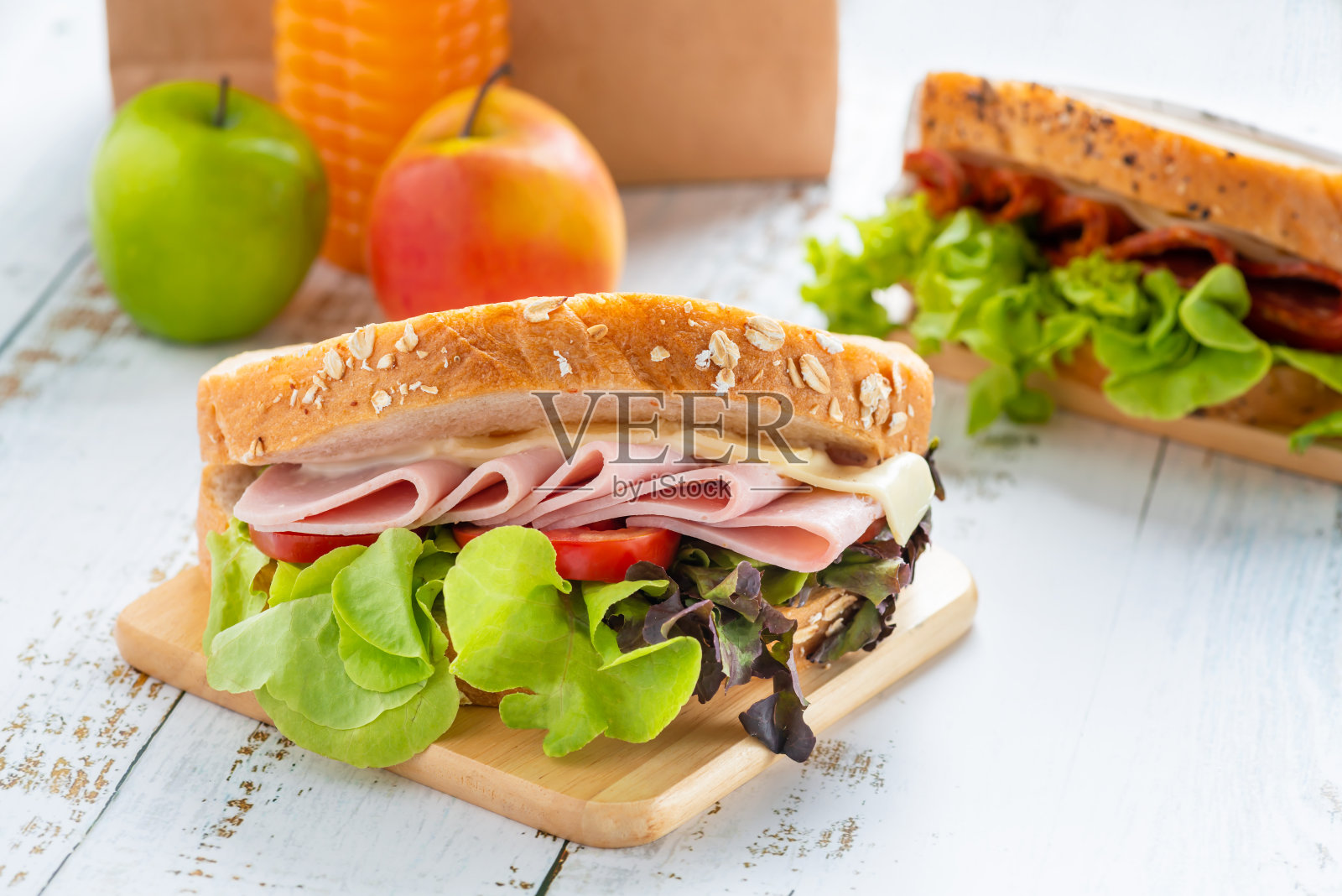 三明治火腿、芝士、蕃茄、生菜配全麦面包和意大利腊肠三明治。橙汁苹果和棕色纸午餐。照片摄影图片