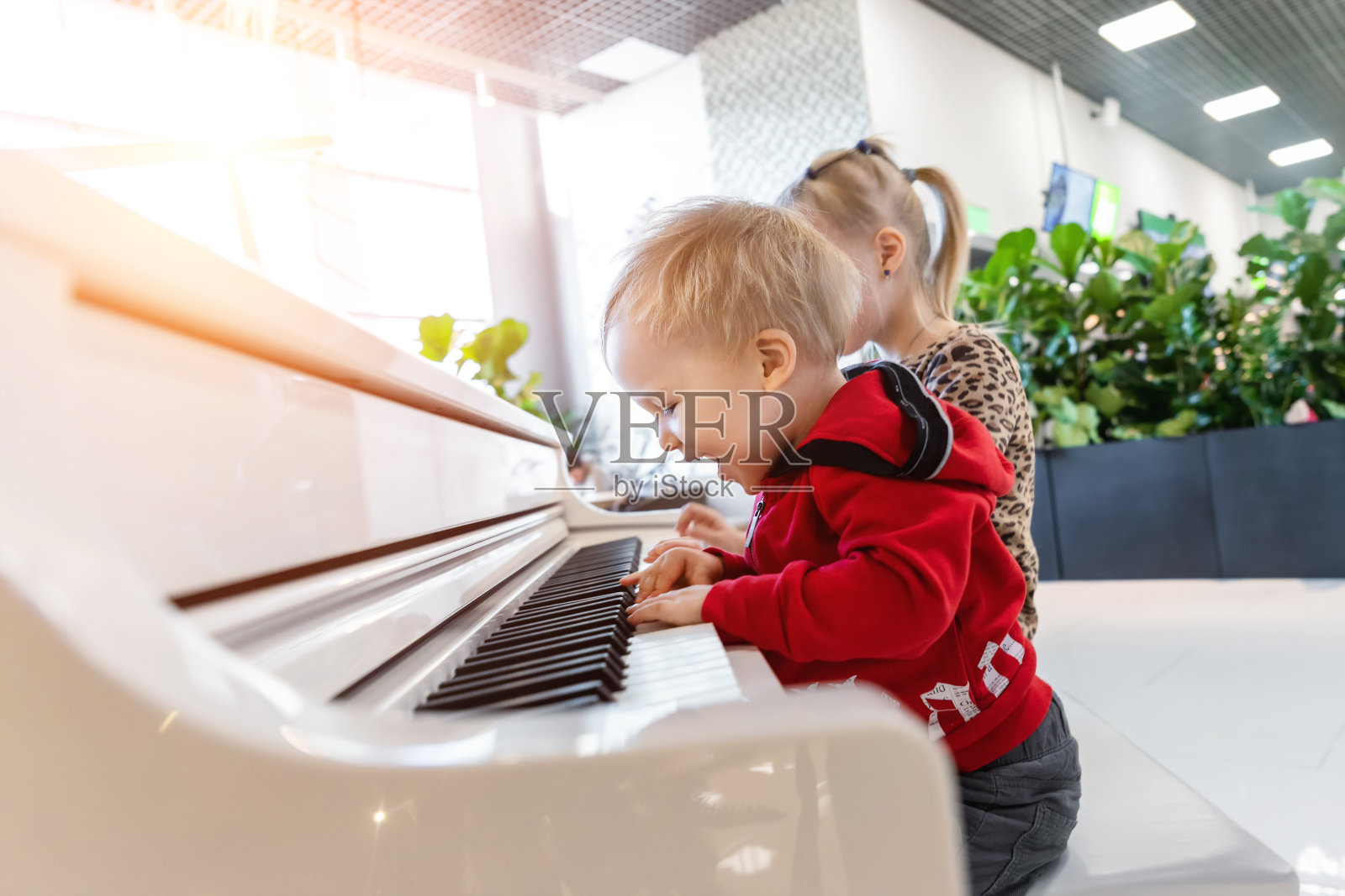 在购物中心室内玩白色大钢琴的可爱幼儿，快乐地唱歌和演奏乐器，快乐的童年照片摄影图片