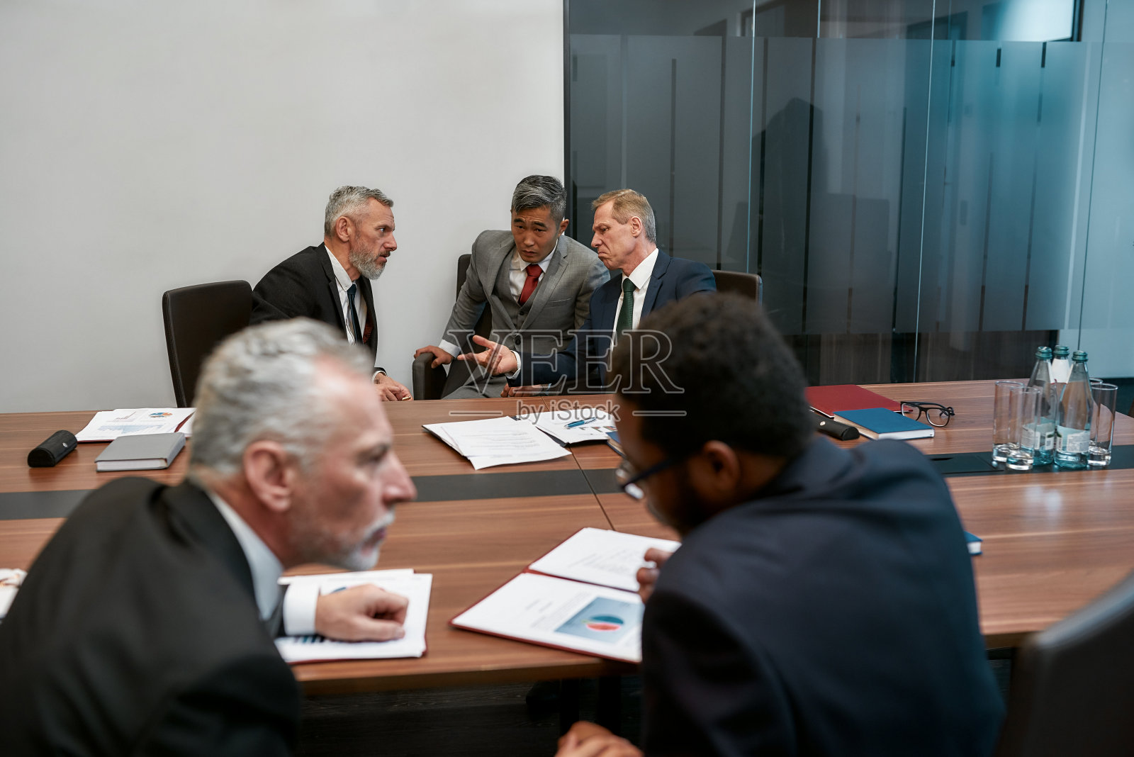 穿着正装的多文化商业人士在现代办公室与合作伙伴开会讨论合同条款照片摄影图片