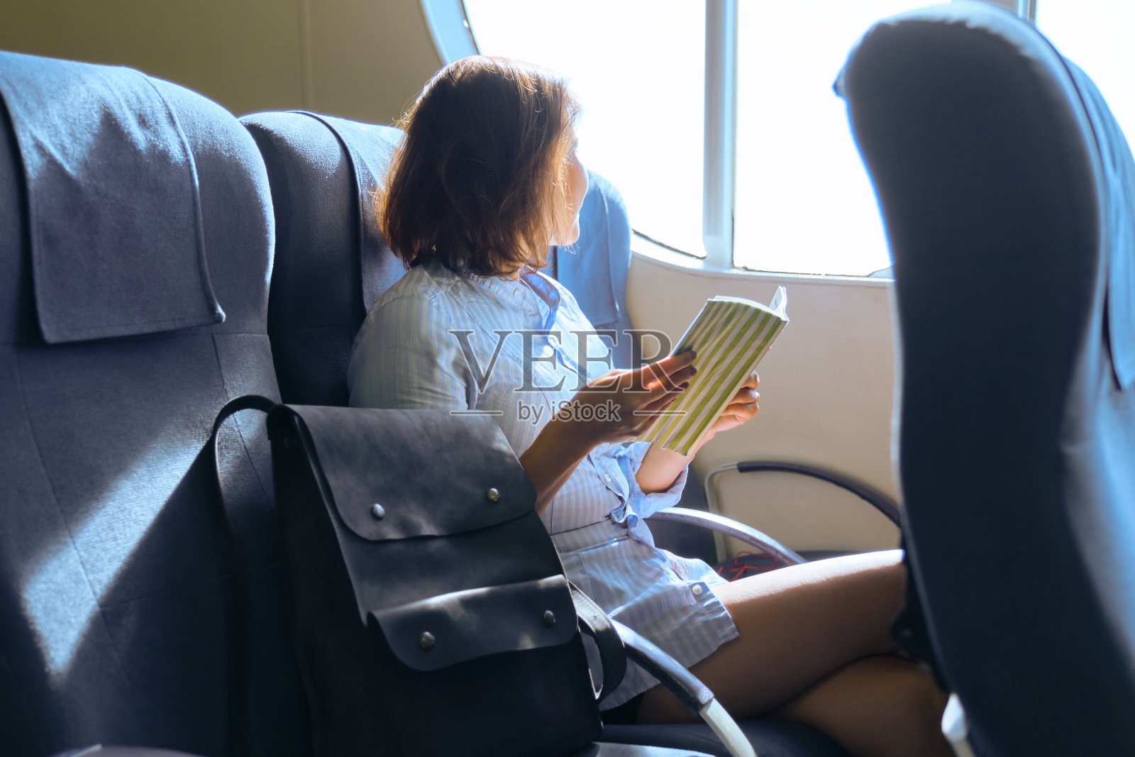 坐在渡轮船舱窗边扶手椅上的成年女性乘客照片摄影图片