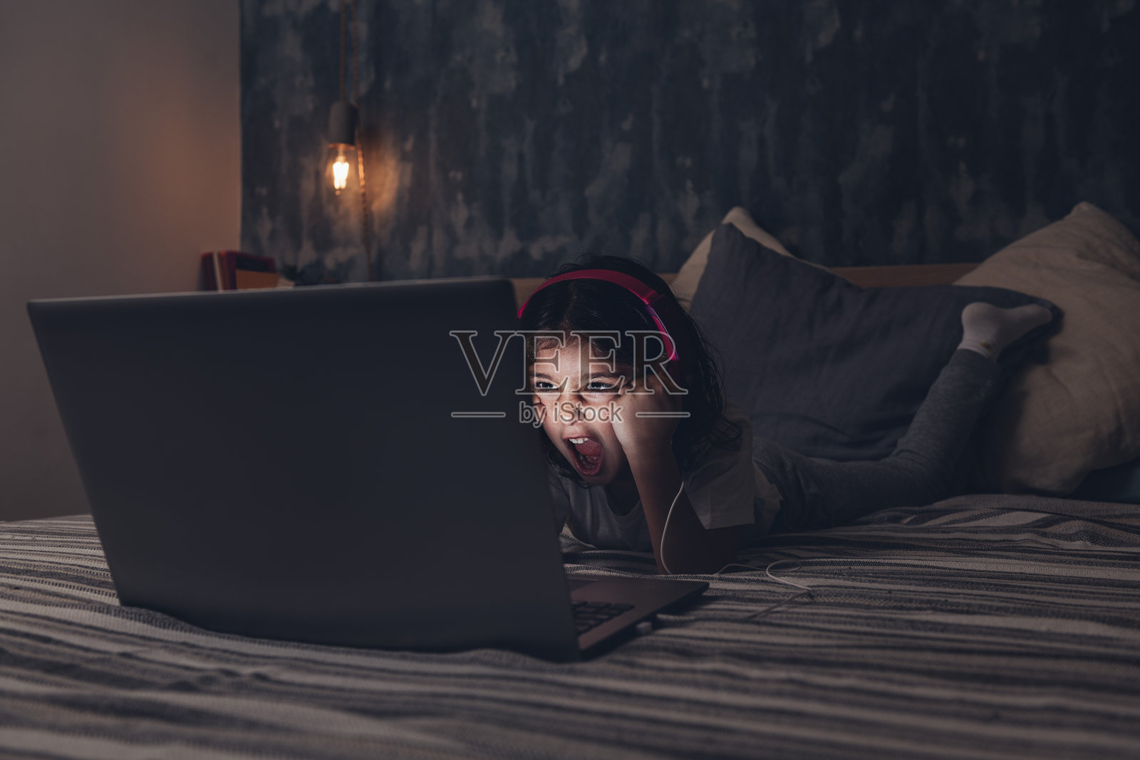 躺在床上对着电脑尖叫的小女孩照片摄影图片