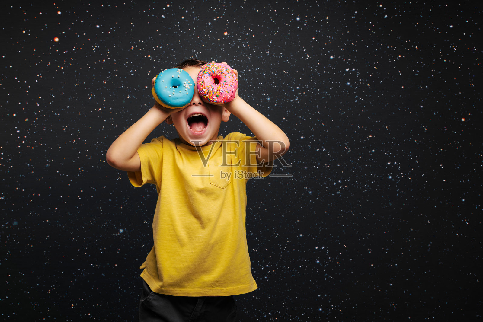 高兴的可爱男孩在黑色背景墙上玩甜甜圈玩得很开心照片摄影图片