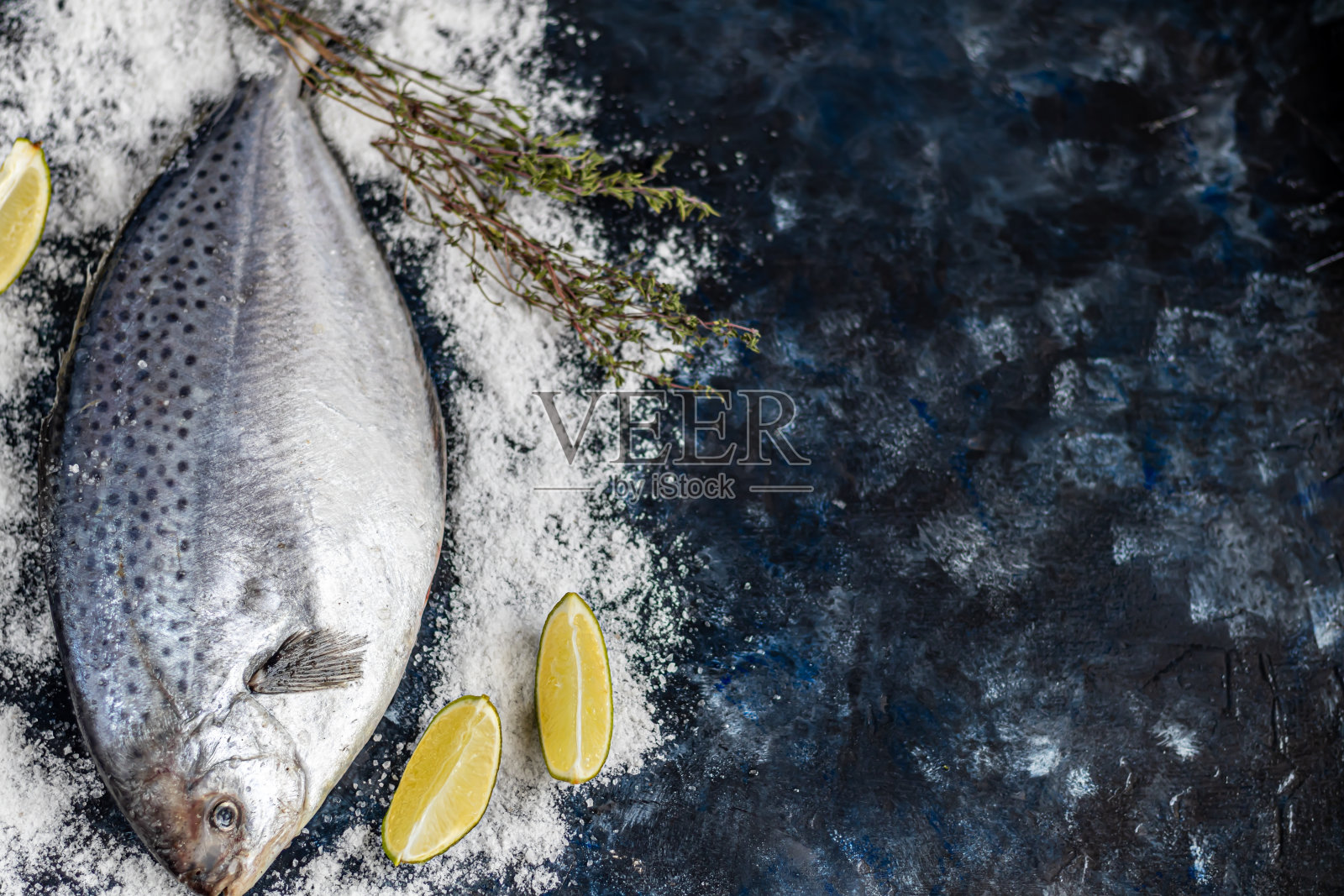 海味鲜美的鱼在黑暗的背景。冷冻产品。鱼与芳香的香草，香料和蔬菜-一个健康饮食的概念，饮食或烹饪。照片摄影图片