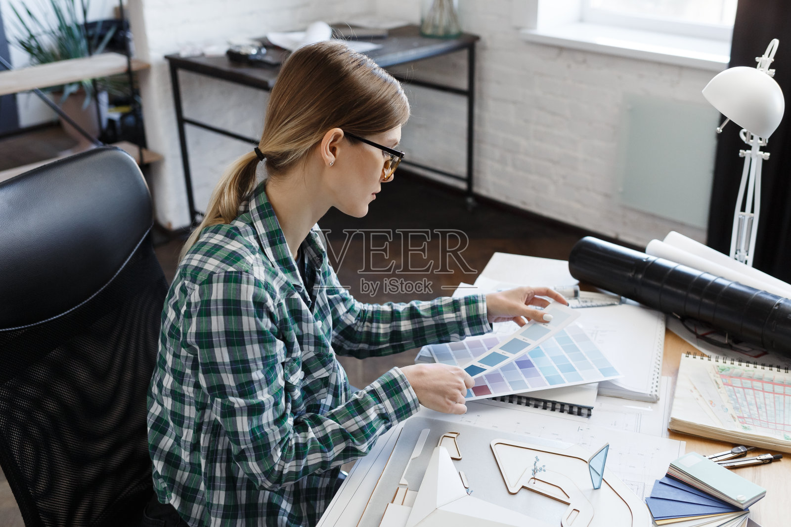 在办公室使用调色板的女室内设计师。建筑师使用色卡为建筑选择颜色，为项目寻找新思路。工作场所的美丽女人肖像照片摄影图片