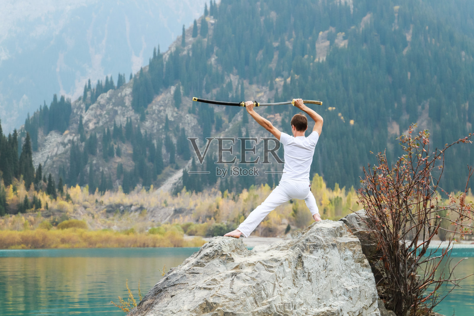 年轻男人站在一块大石头上，手里拿着一把日本刀照片摄影图片