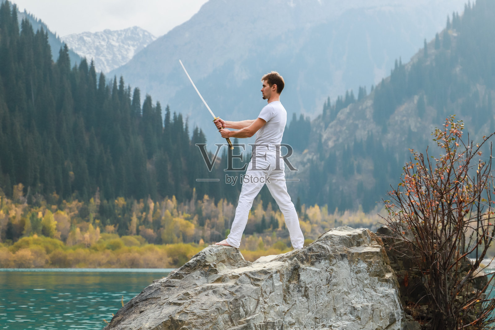 年轻男人站在一块大石头上，手里拿着一把日本刀照片摄影图片