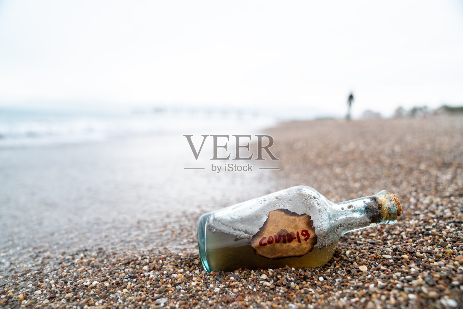 带有Covid-19标签的沙滩上海浪的玻璃瓶照片摄影图片