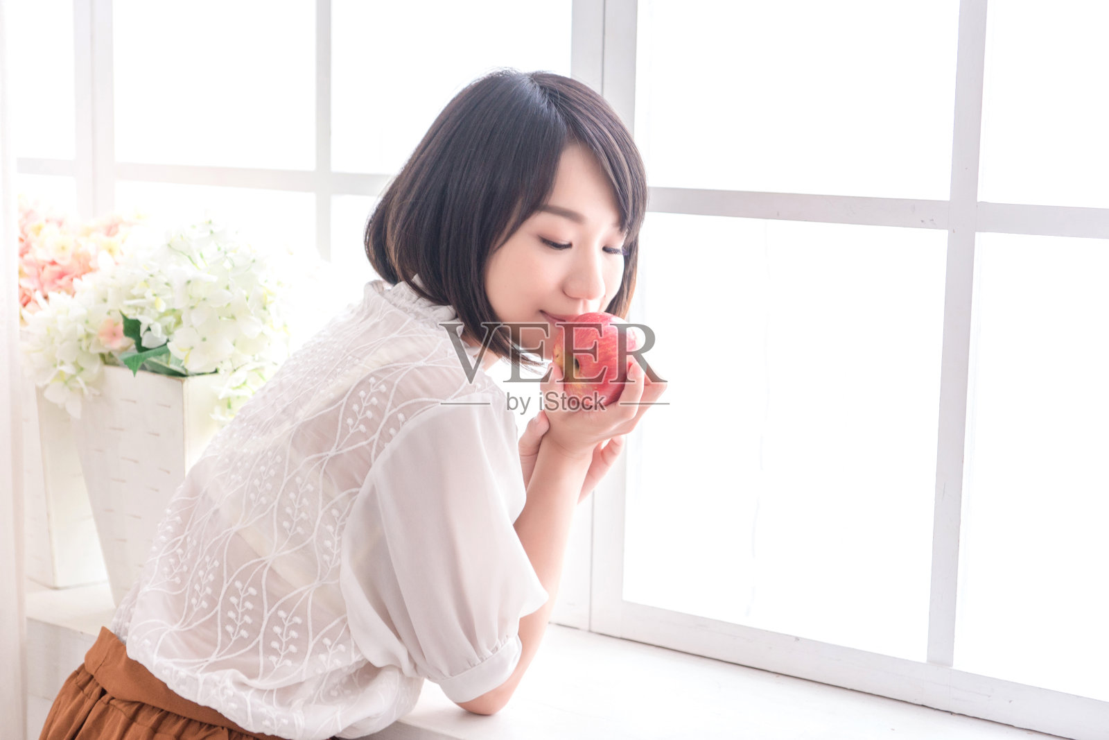 美丽的亚洲女孩在房子里拿着苹果，教育、健康或创业概念，现代办公室或客厅有复制空间照片摄影图片