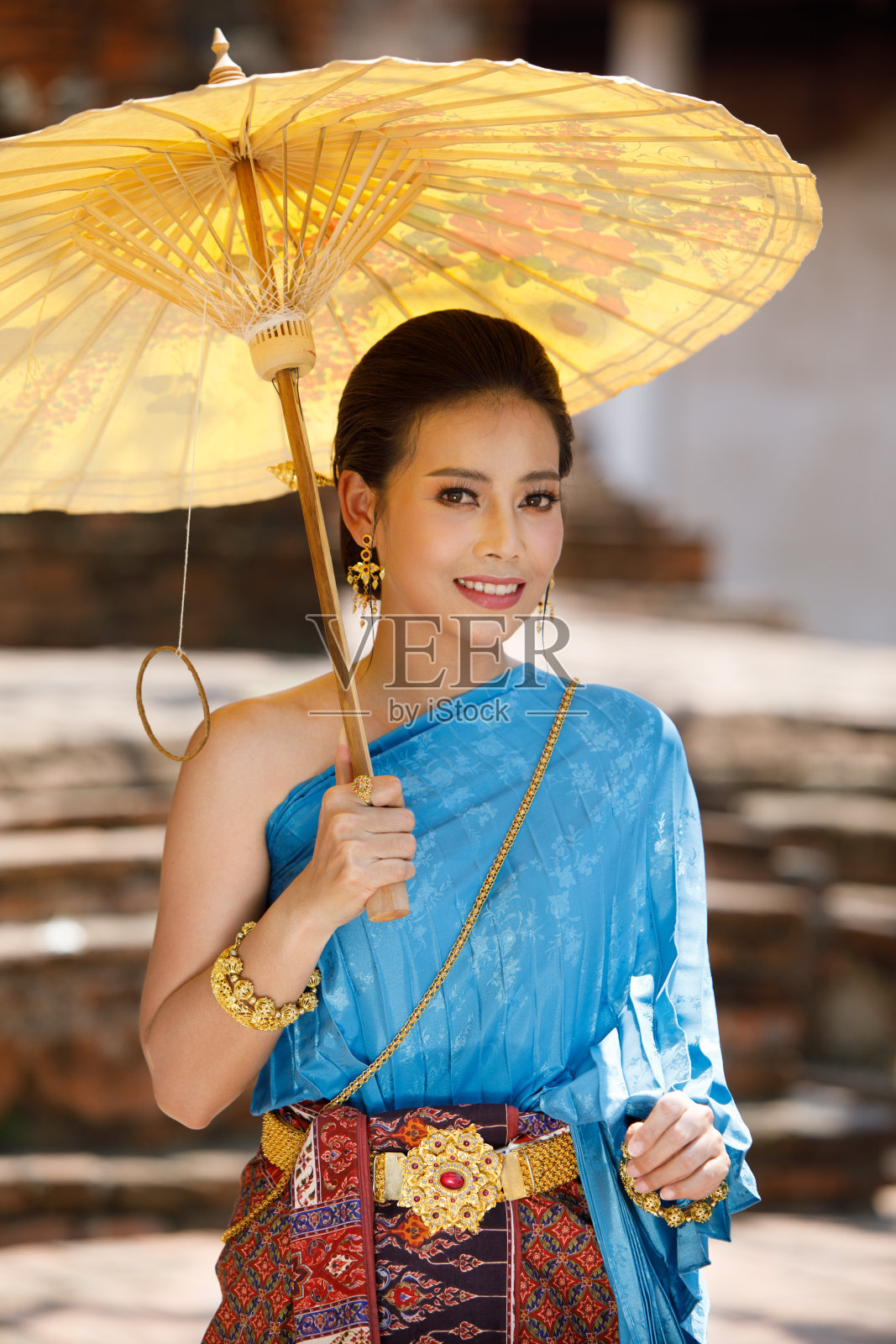 穿着泰国传统服装，在泰国寺庙里拿着黄色雨伞的泰国女性照片摄影图片