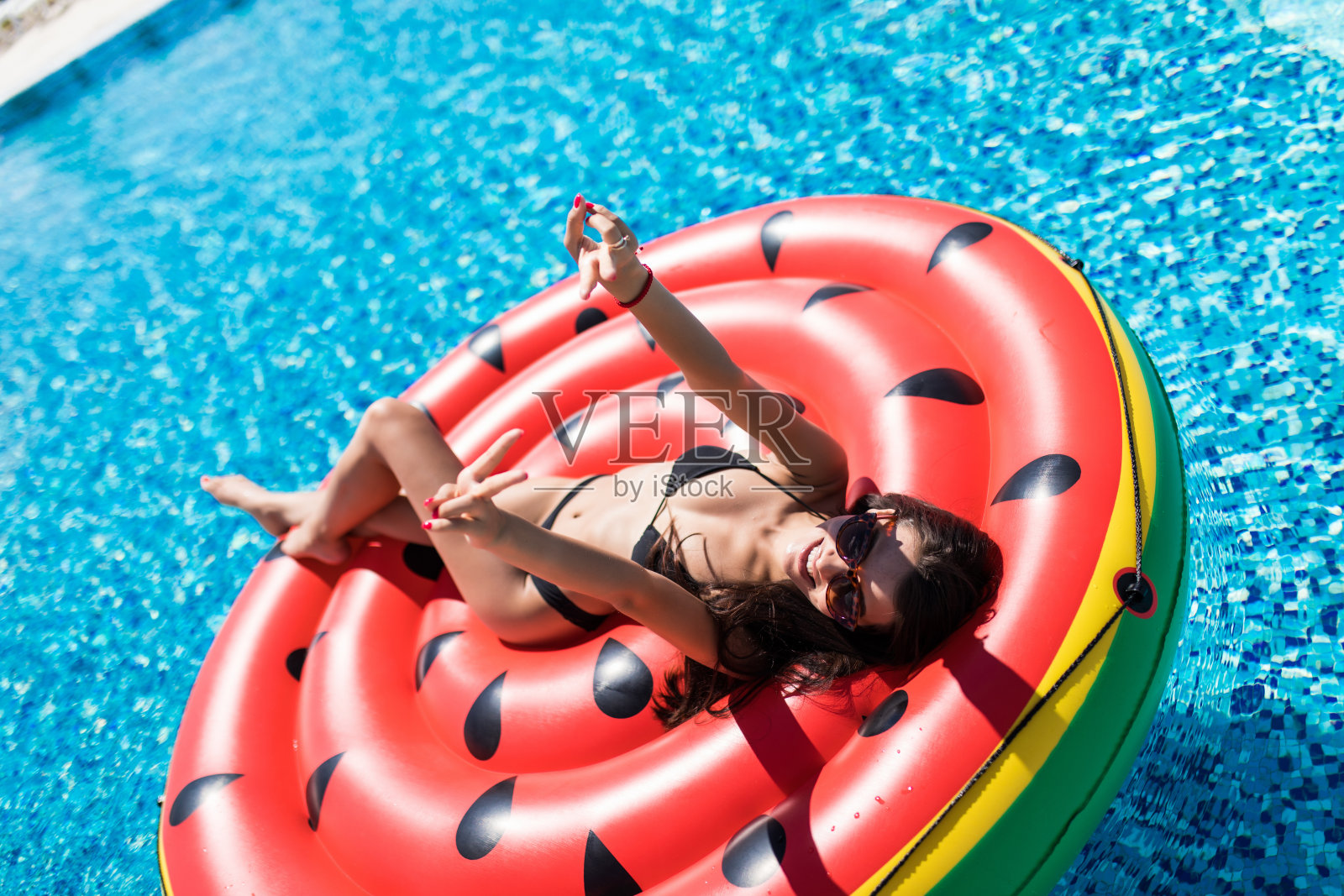在泳池里拿着充气西瓜晒日光浴的漂亮女人照片摄影图片