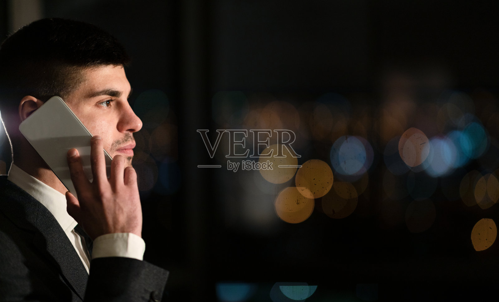 在办公室窗边用手机通话的商人（侧面）照片摄影图片