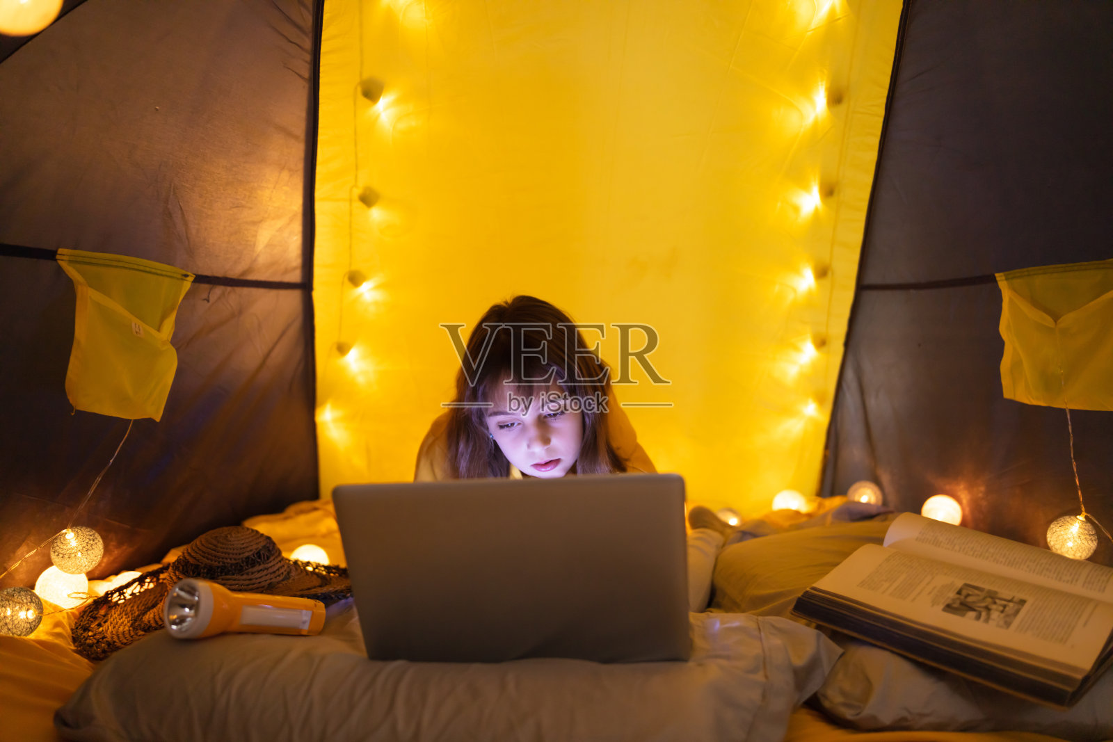 一个11岁的小女孩在客厅里她自制的帐篷下使用笔记本电脑。照片摄影图片