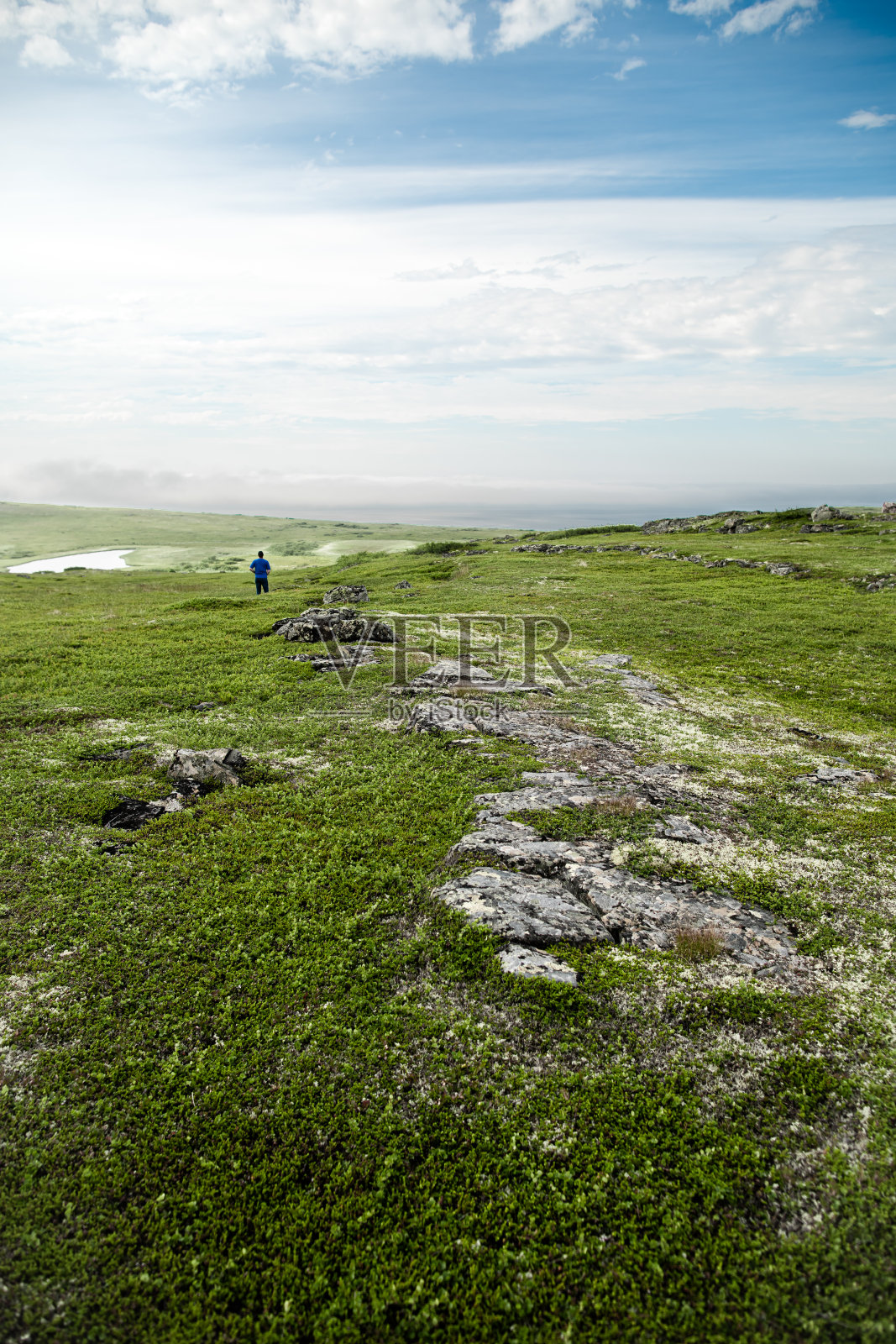 看到绿色的山丘和一个孤独的游客在上面的池塘照片摄影图片