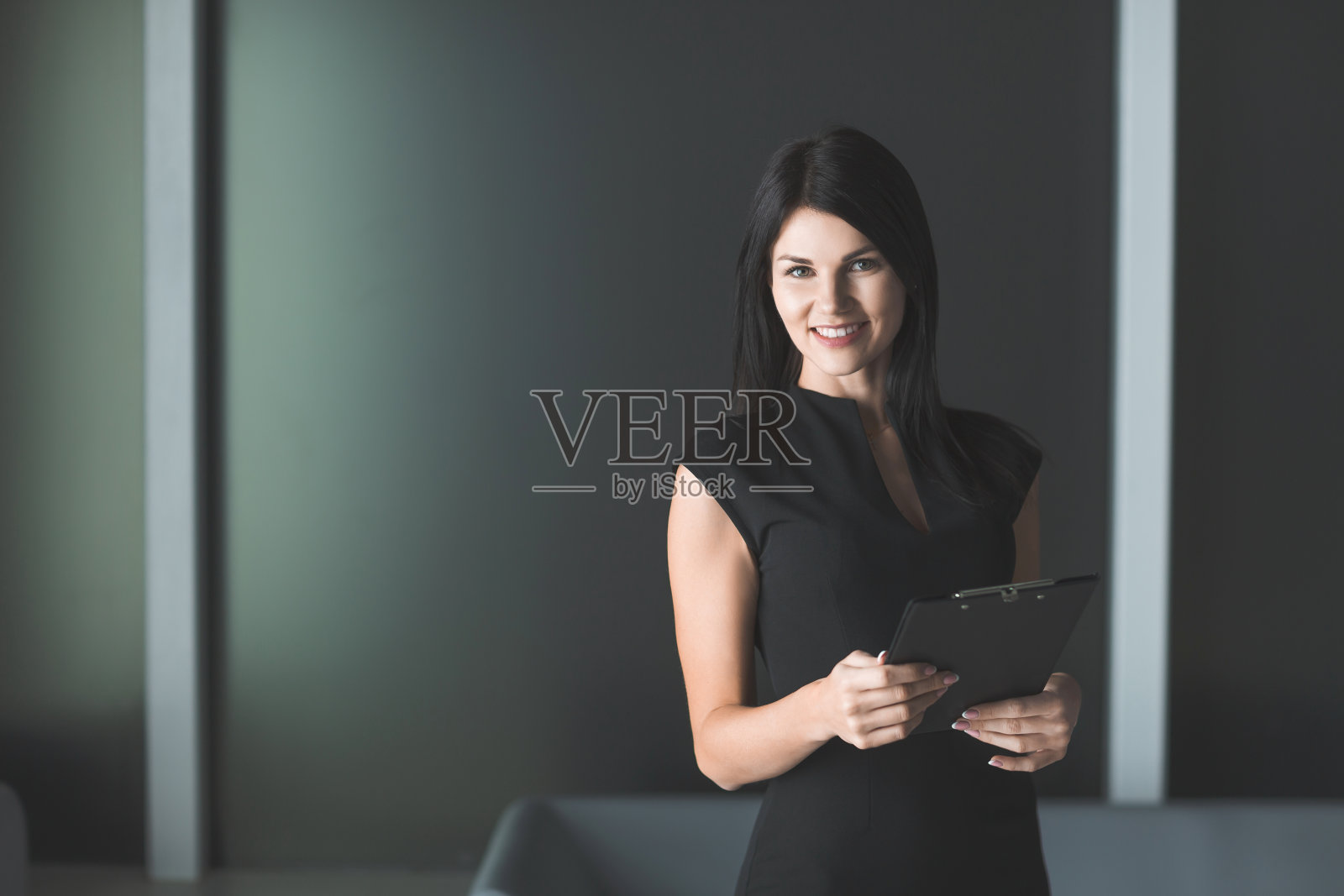 带着写字板站在办公室里的女商人。照片摄影图片