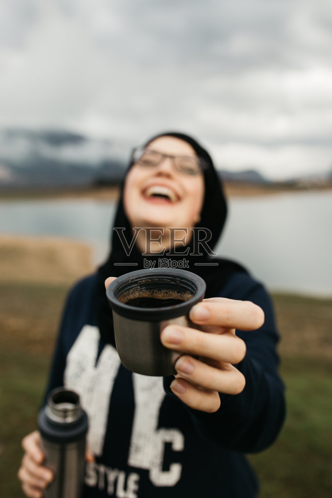 戴着头巾的快乐女人在雾蒙蒙的早晨在湖光山色中喝咖啡照片摄影图片