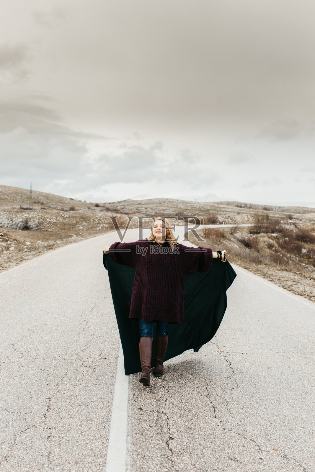 年轻女子的肖像，头发在风中飘动。她穿着一件皮夹克，背景是模糊的自然和道路。旅游秋色，大气瞬间。照片摄影图片