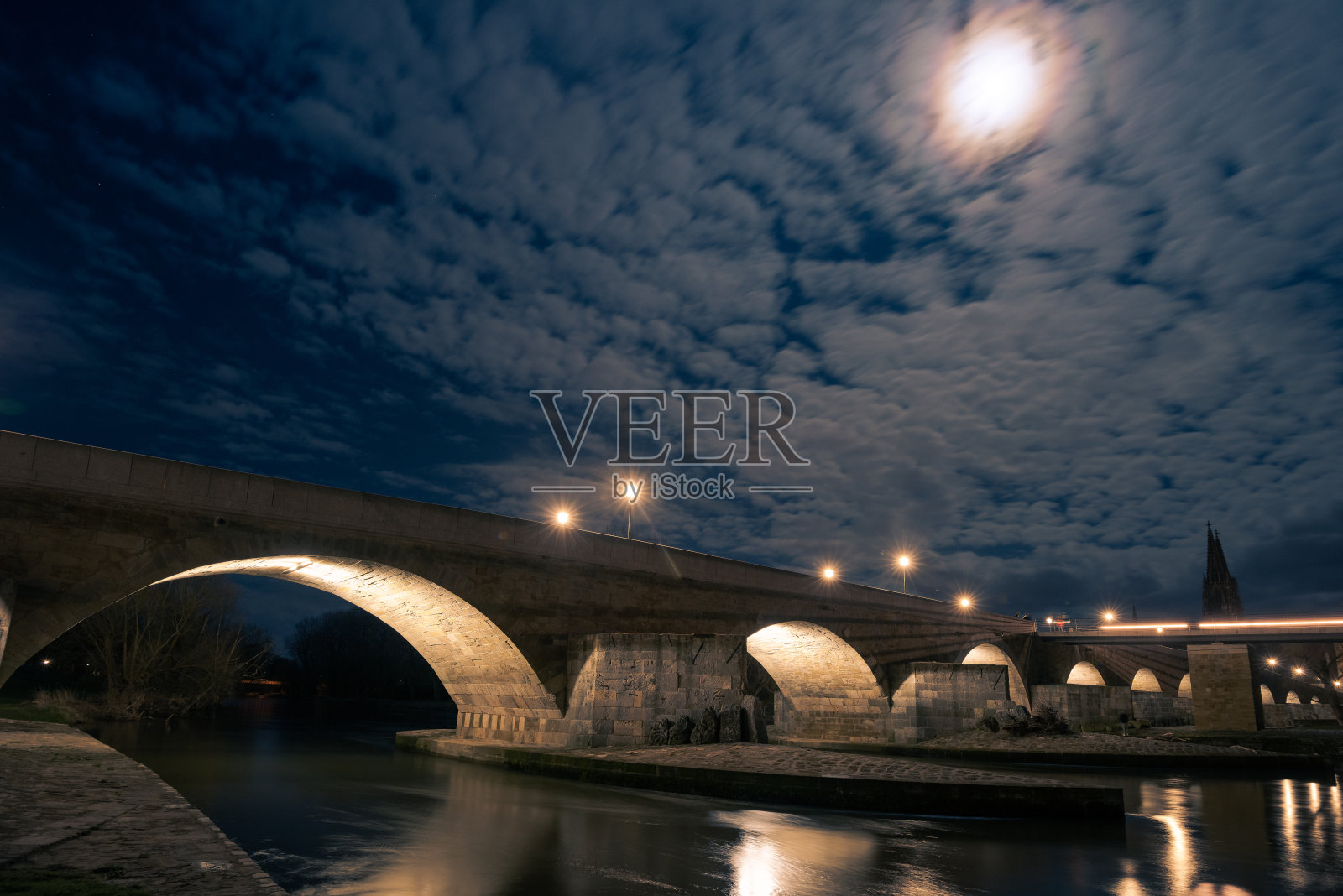 巴伐利亚州雷根斯堡的历史悠久的发光石桥，在满月的夜晚以大教堂为背景照片摄影图片