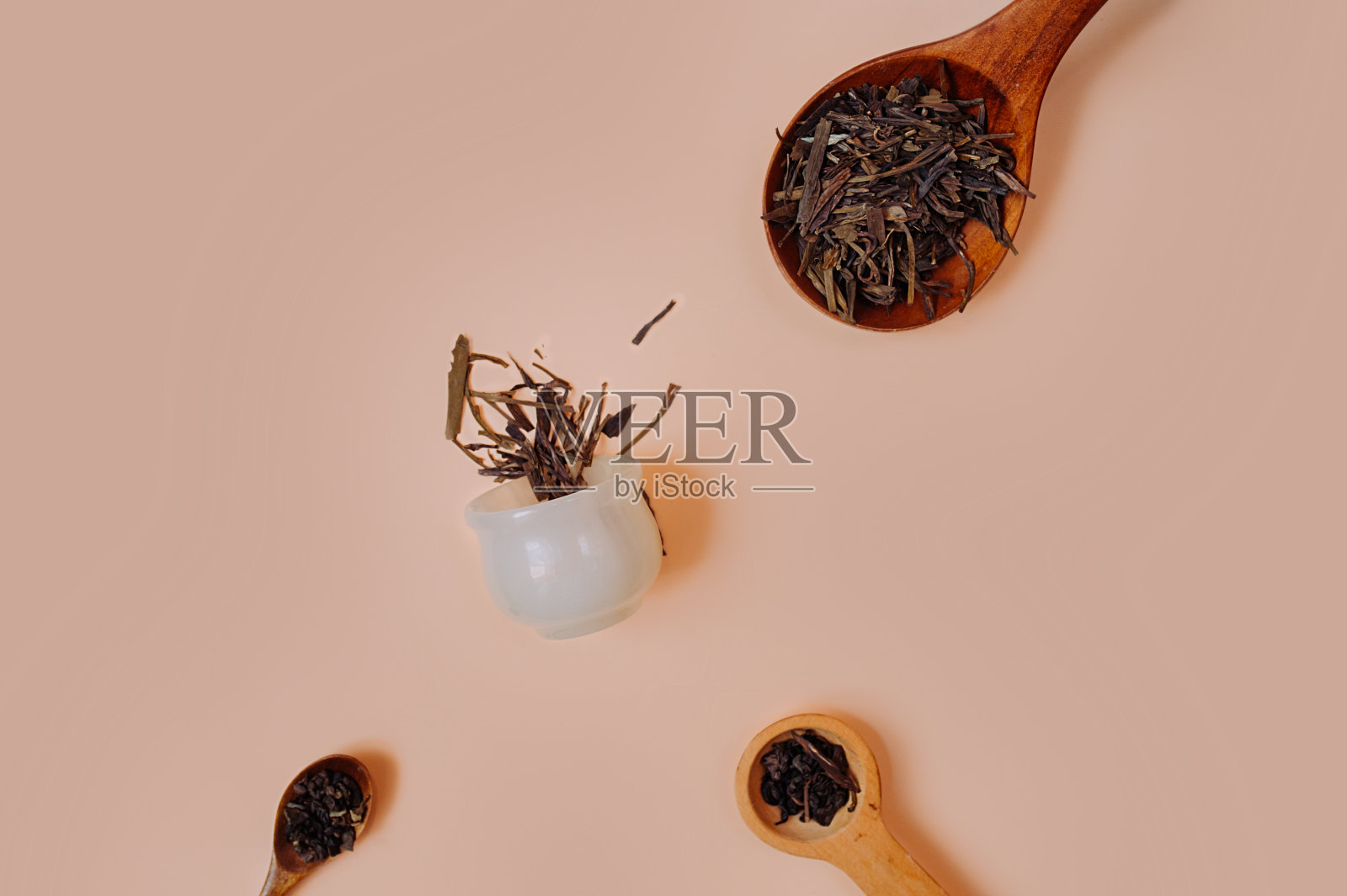 关于茶和喝茶的软粉色照片。茶粒和茶叶放在不同大小的木勺上，干茶从一个白色的石头杯子里倒出来，中国式的。照片摄影图片