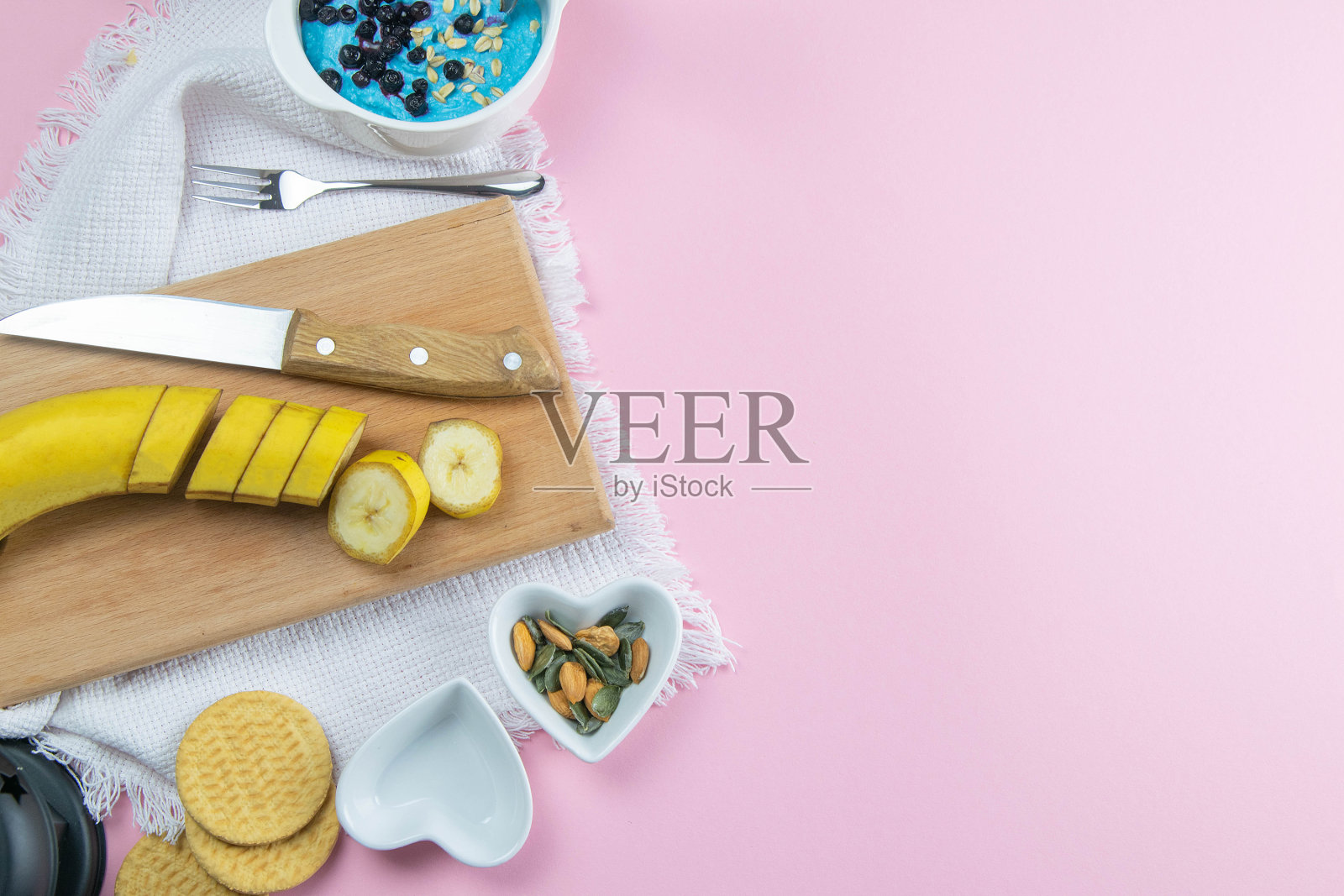 木盘上放着香蕉片，沙拉碗旁边放着杏仁和南瓜子照片摄影图片