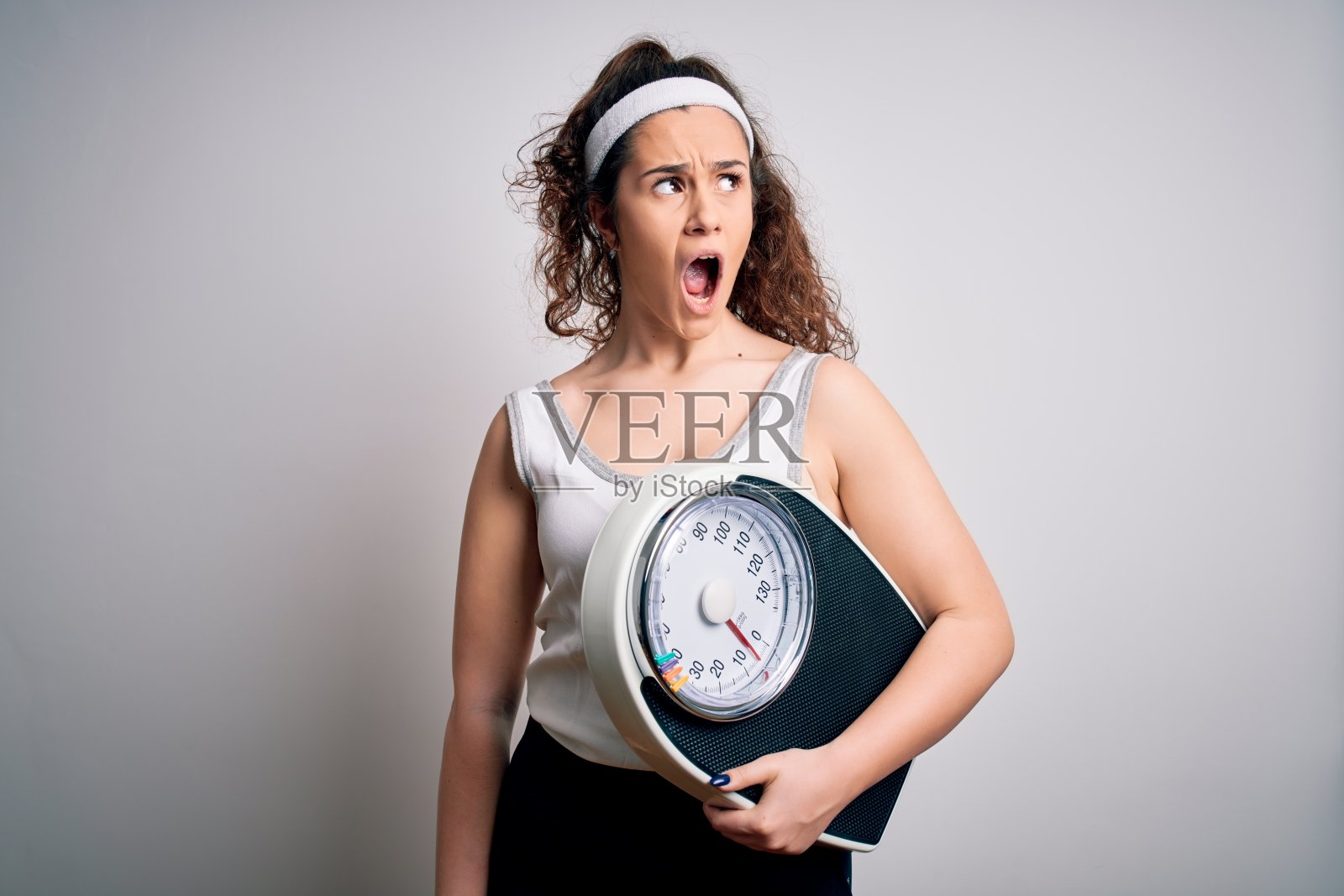 拿着体重秤的年轻卷发美女，愤怒尖叫照片摄影图片