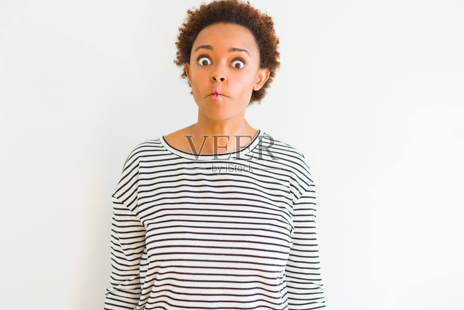 年轻漂亮的非裔美国妇女穿着条纹毛衣，白色背景，用嘴唇做鱼脸，疯狂而滑稽的姿势。有趣的表情照片摄影图片