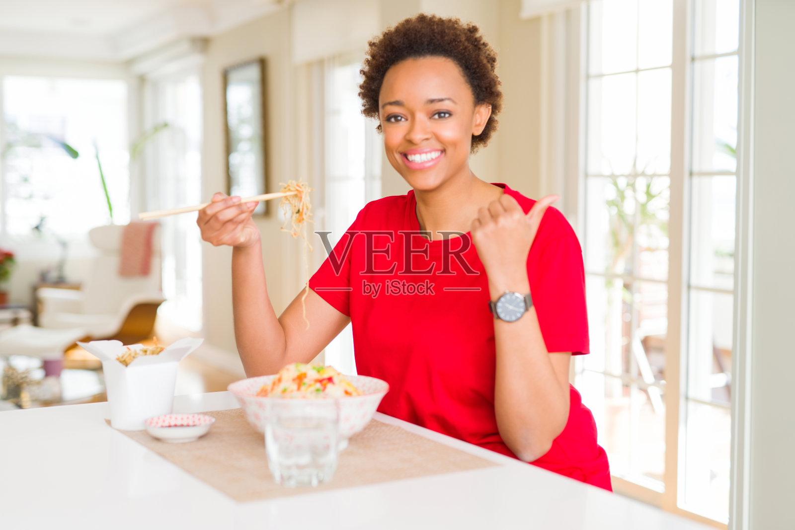 年轻的非裔美国妇女在家吃亚洲食物，竖起大拇指照片摄影图片