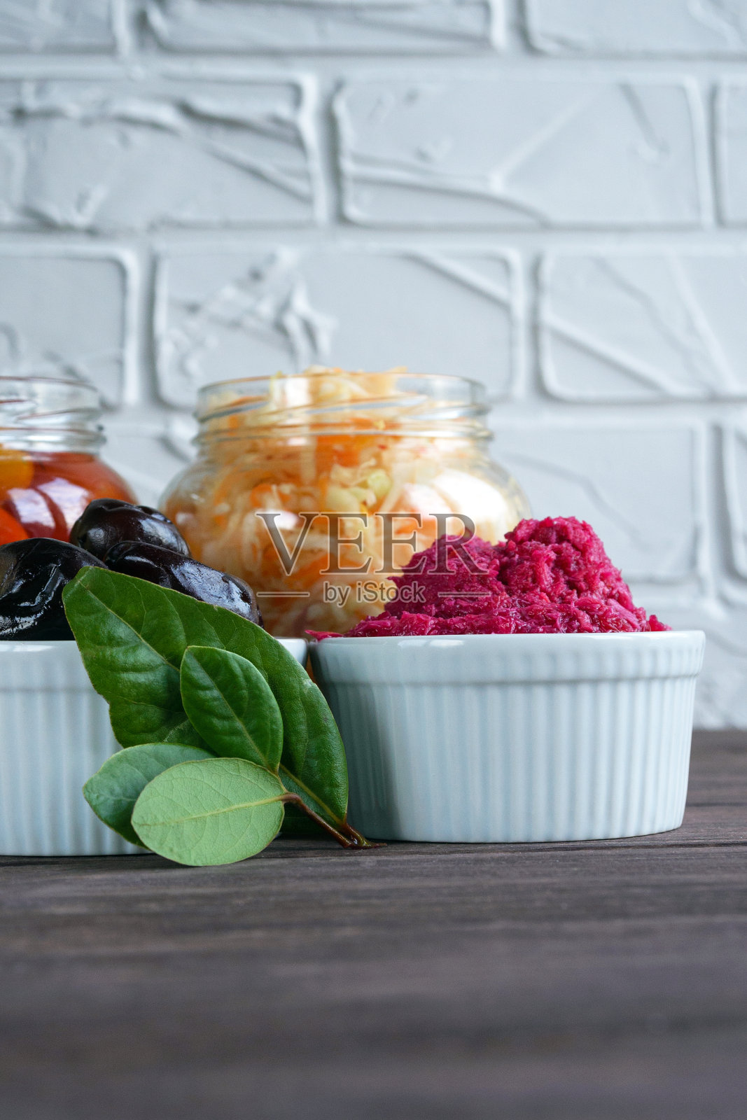 树枝上的绿色月桂叶背景为发酵食品。白底上有泡菜、腌番茄、腌李子和辣山葵。照片摄影图片