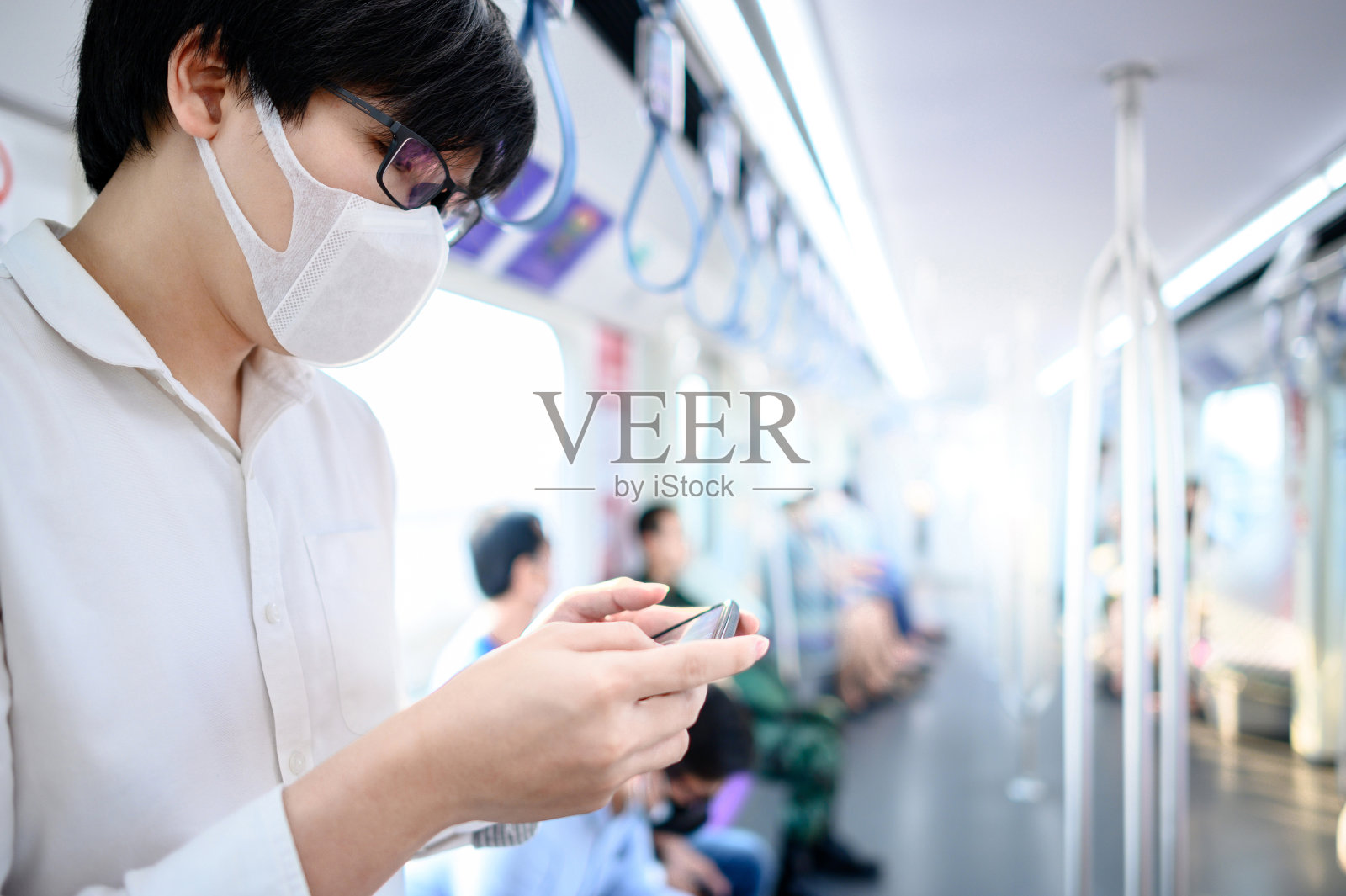 戴口罩的亚洲男人在轻轨上用手机照片摄影图片