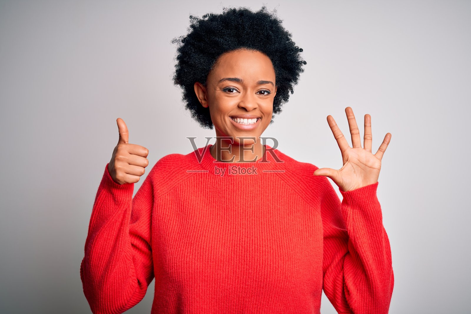 穿着红色休闲毛衣的年轻漂亮的非裔美国卷发女性，面带自信和快乐的微笑，用手指向上展示数字六照片摄影图片