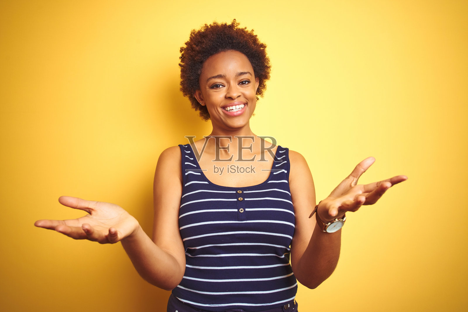 美丽的非洲裔美国妇女穿着夏天的t恤在孤立的黄色背景微笑着提供帮助和接受的手。照片摄影图片