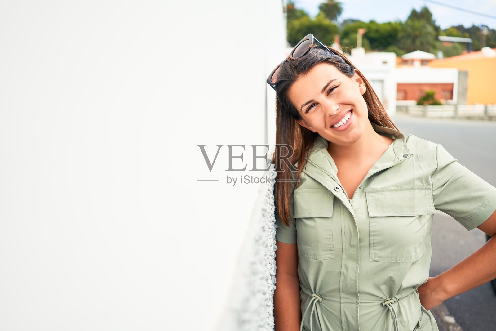 美丽的女孩靠在白色的墙壁上，年轻友好的女人在一个阳光明媚的夏天快乐地微笑照片摄影图片