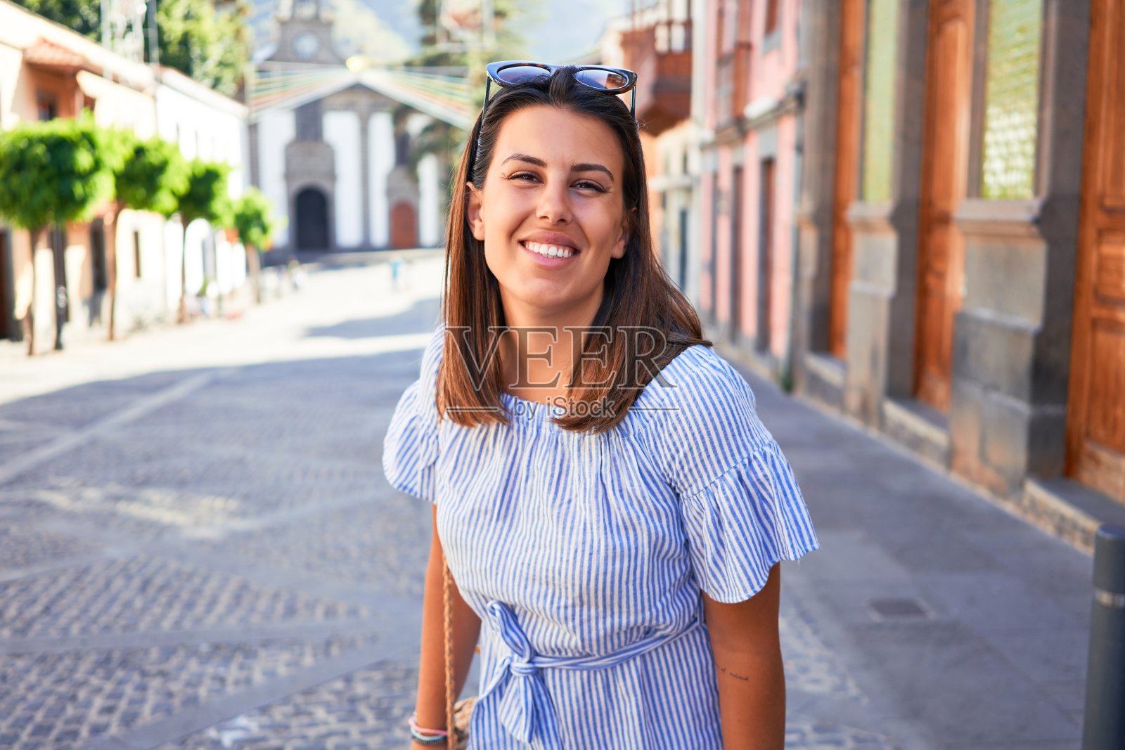 在一个阳光明媚的日子里，年轻美丽的女人走在浪漫的村庄的街道上照片摄影图片