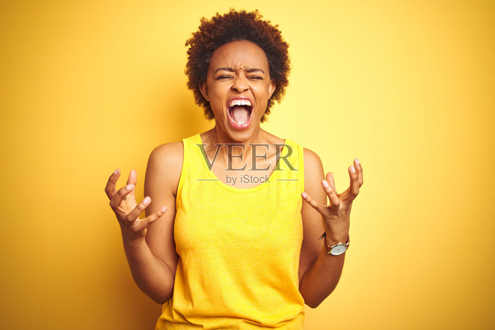 穿着夏日T恤的非裔美国女人，黄色背景，疯狂地喊叫，手臂抬起，表情充满攻击性。沮丧的概念。照片摄影图片