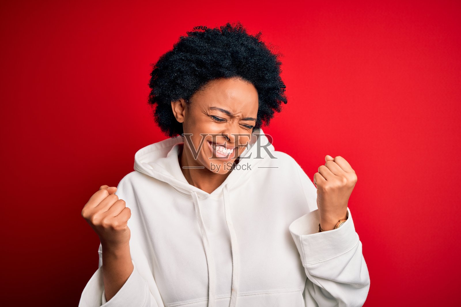 年轻漂亮的非裔美国女运动员，卷发，身穿运动服，举起双臂，笑容满面，为成功欢呼照片摄影图片