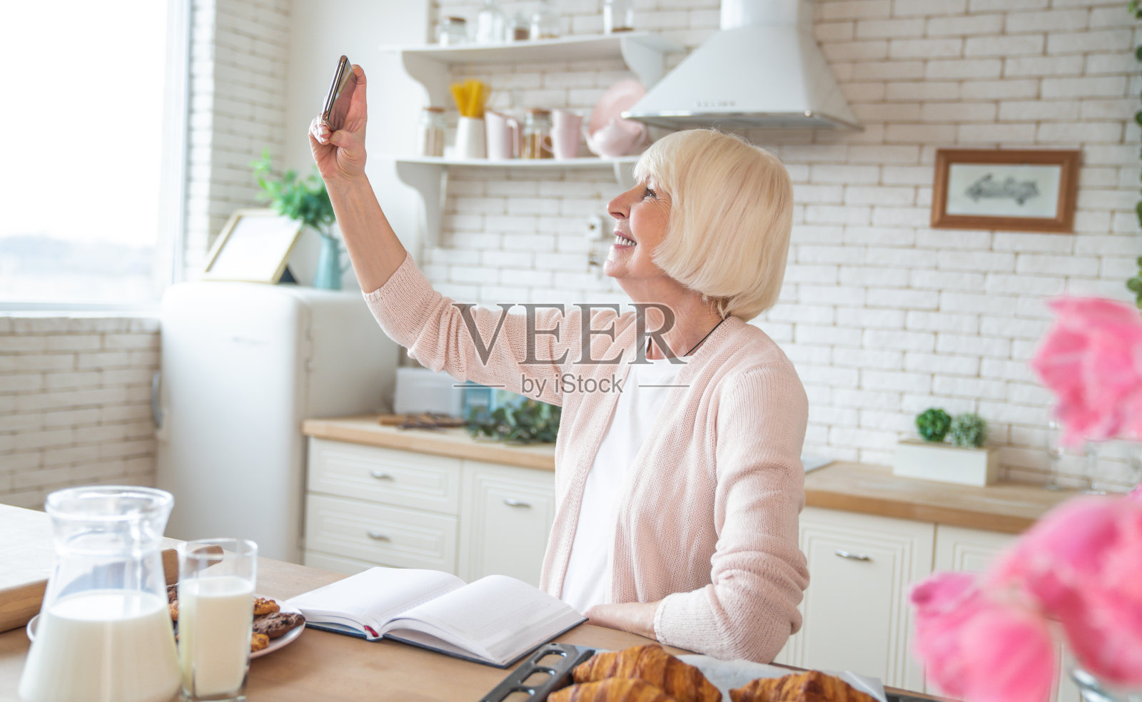 老妇在厨房烹饪，用智能手机自拍照片摄影图片