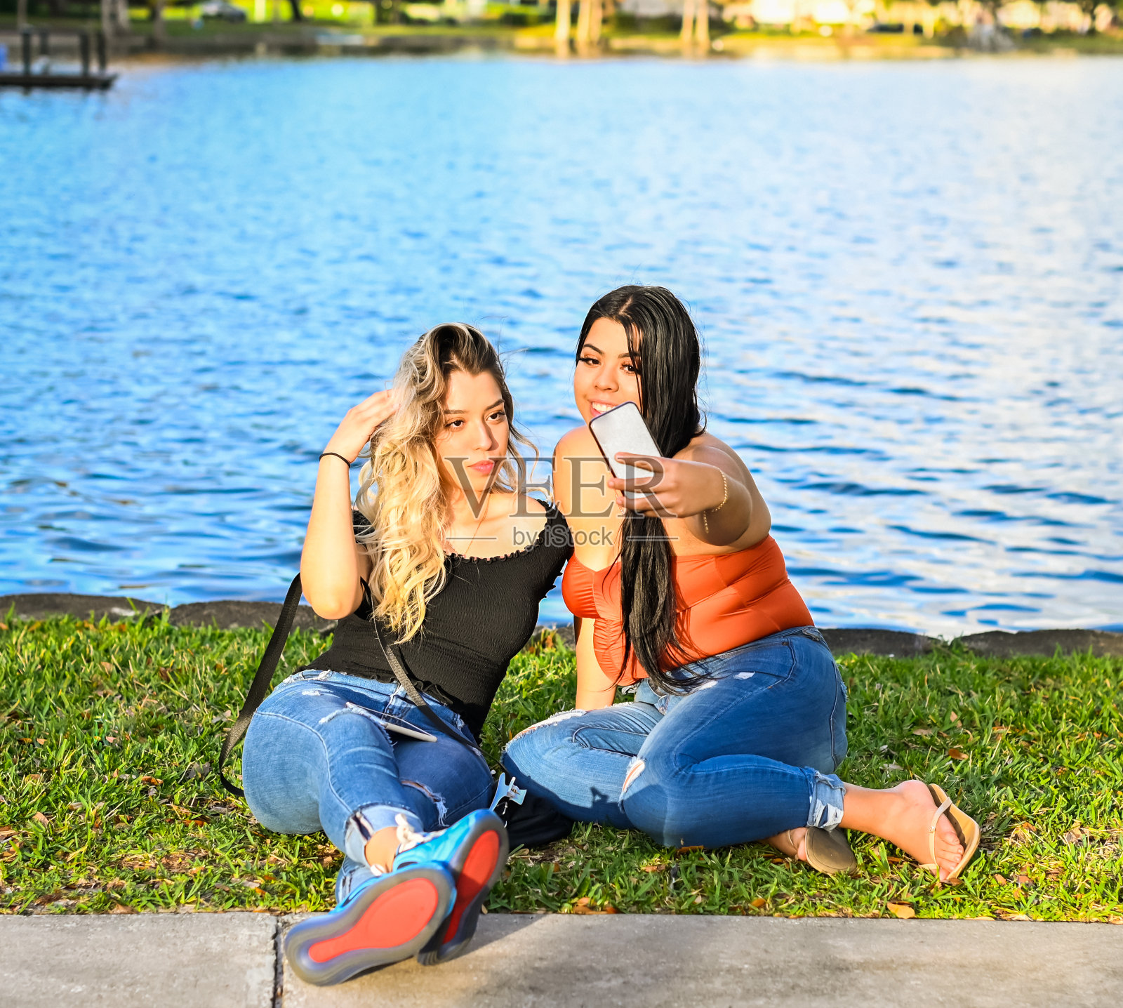 两个年轻的拉丁妇女坐在草地上拿着手机照片摄影图片