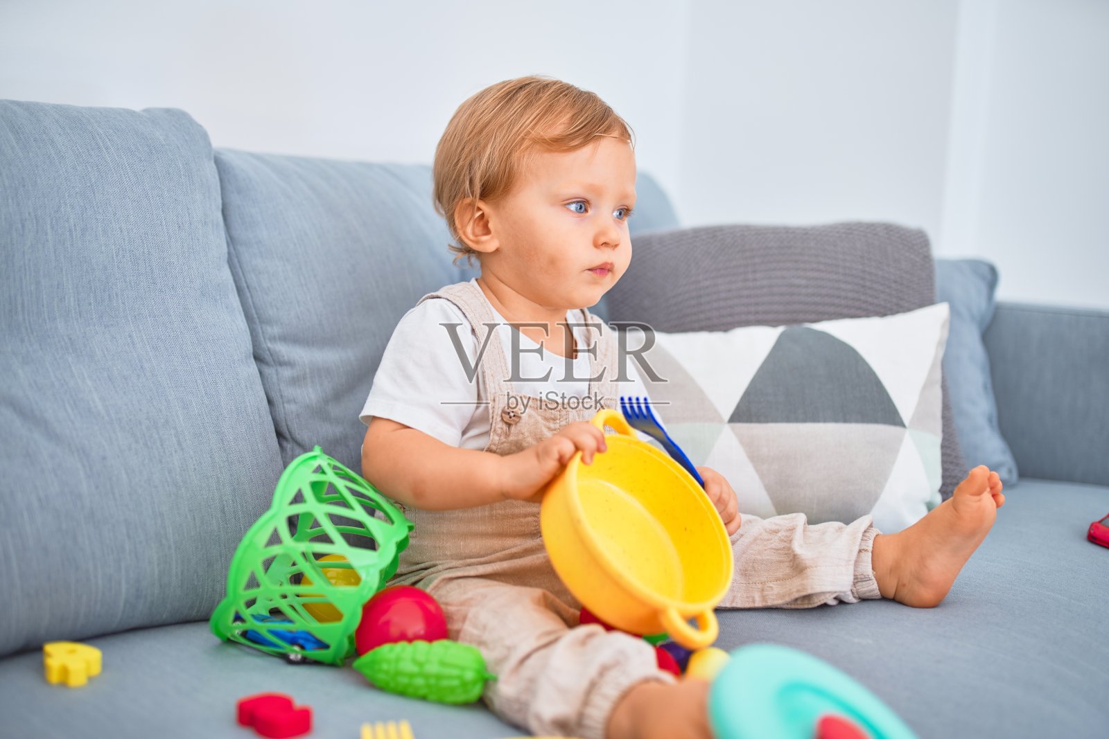 可爱的金发幼儿坐在沙发上玩塑料餐具玩具照片摄影图片