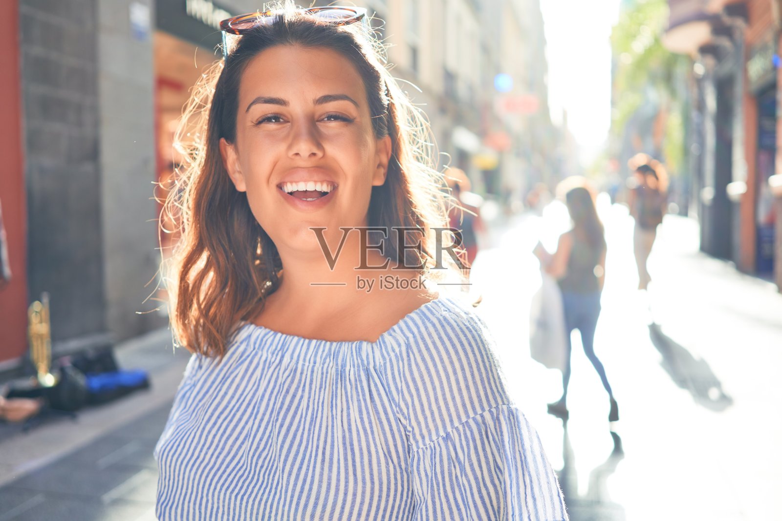 在一个阳光明媚的夏天，年轻美丽的女人快乐地走在城市的街道上照片摄影图片