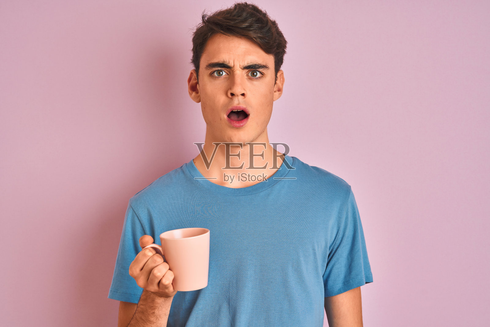 青少年男孩喝咖啡，粉色背景，面露惊讶照片摄影图片