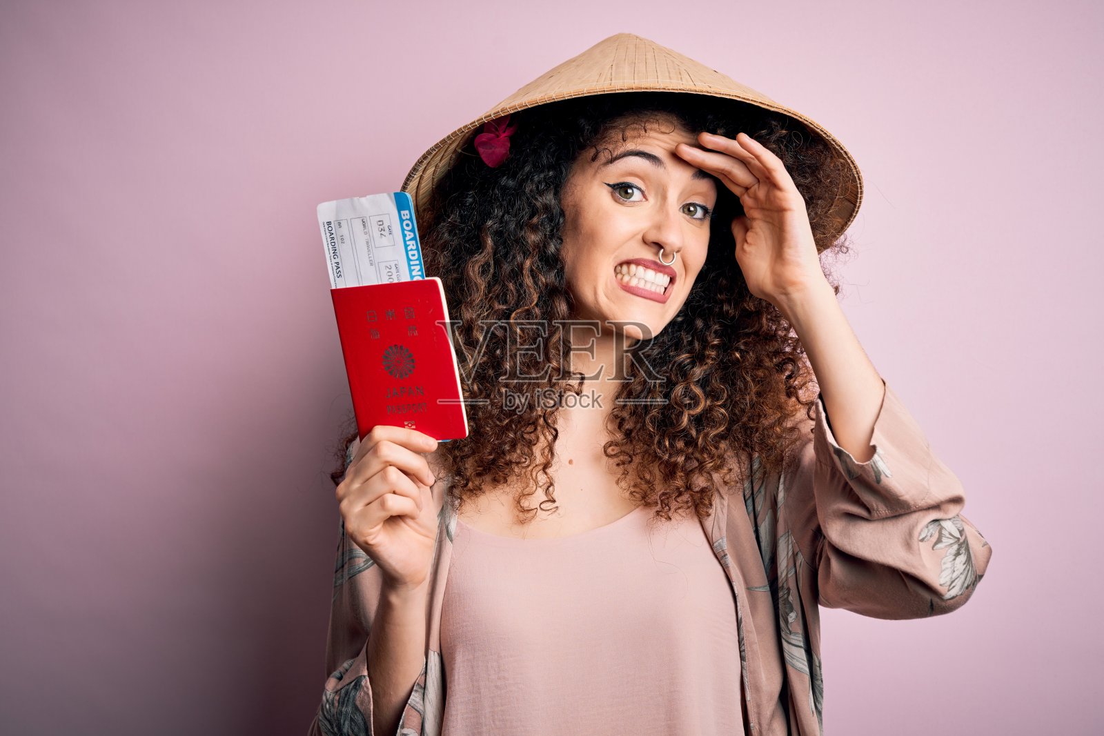 美丽的卷发、有穿孔的游客女子戴着亚洲帽子，拿着日本护照，手放在头上感到压力，因羞耻和惊讶而震惊，愤怒和沮丧。因错误而感到恐惧和不安。照片摄影图片