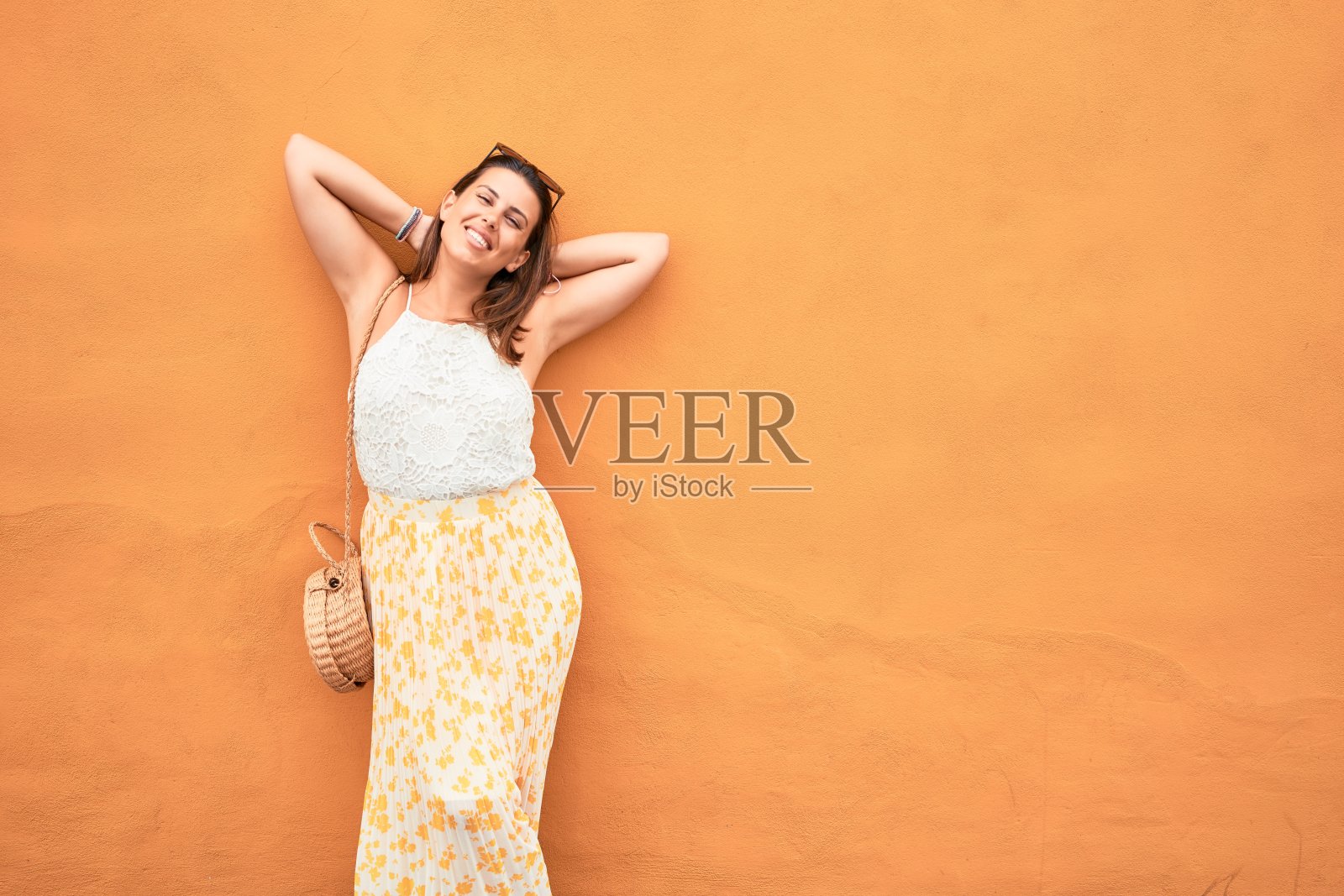 美丽的女孩倚在橘色的墙壁上，年轻友好的女人在一个阳光明媚的夏天快乐地微笑着照片摄影图片