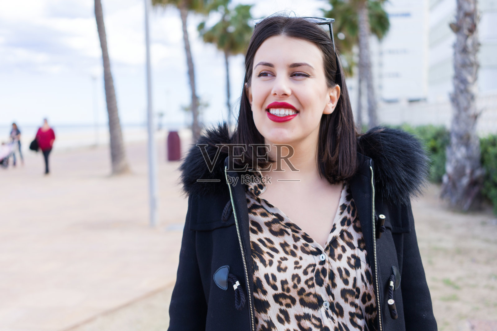 年轻漂亮的女人戴着太阳镜和外套走在人行道上照片摄影图片